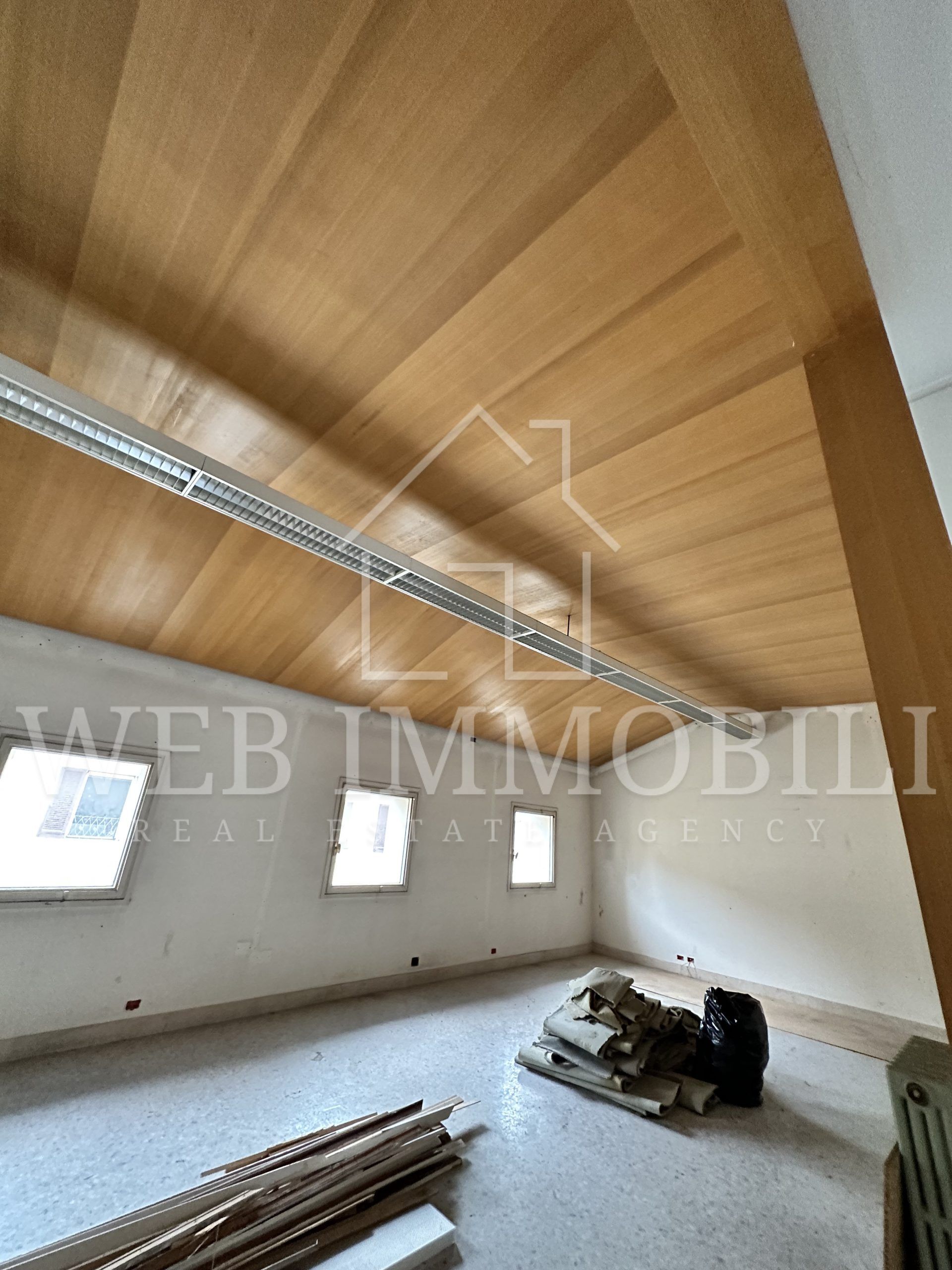 Stanza interna con soffitto in legno, piccole finestre e detriti sul pavimento.