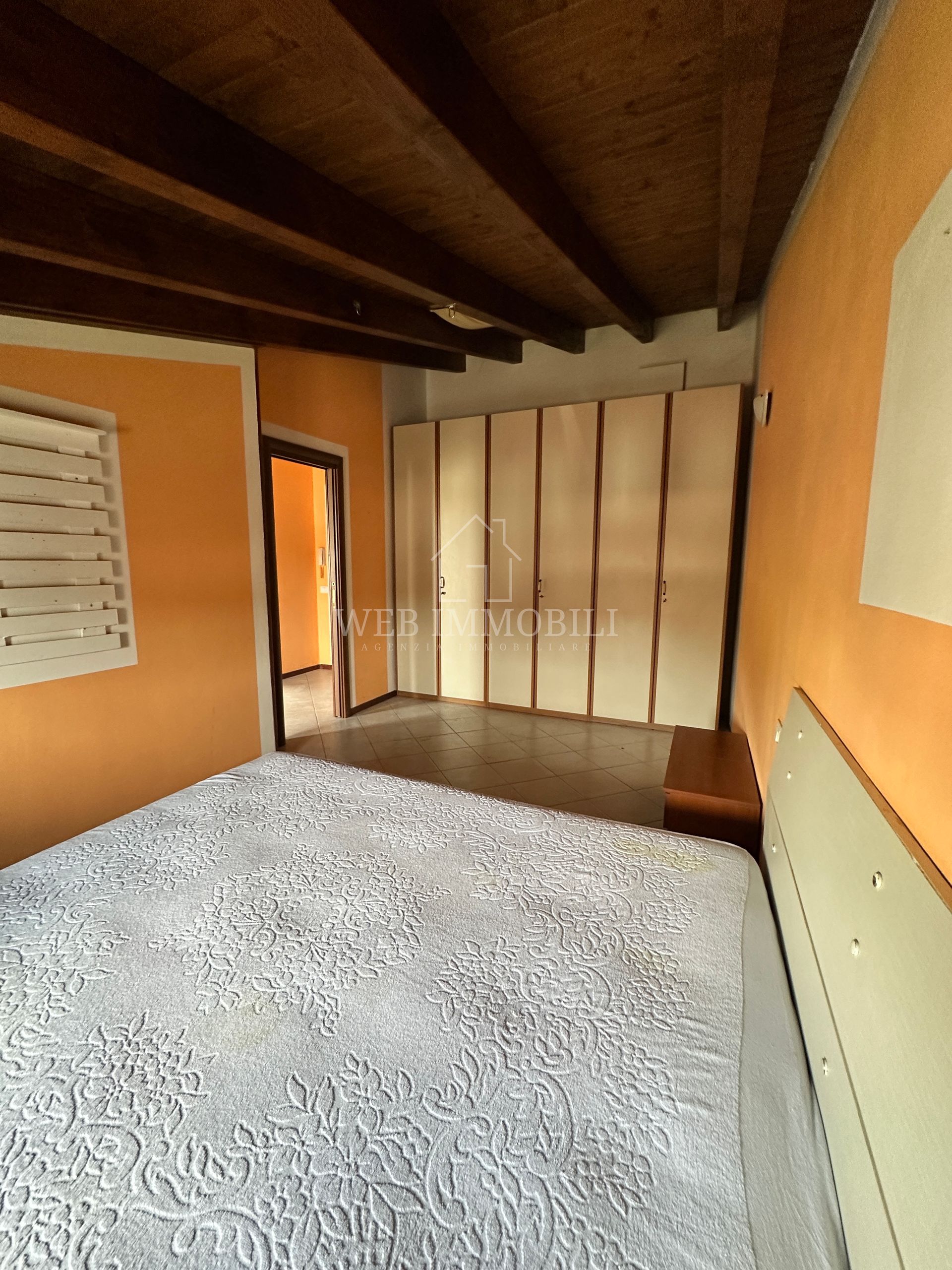Camera da letto con pareti arancioni, soffitto in legno, ampio armadio a muro e letto con piumone grigio a fantasia.