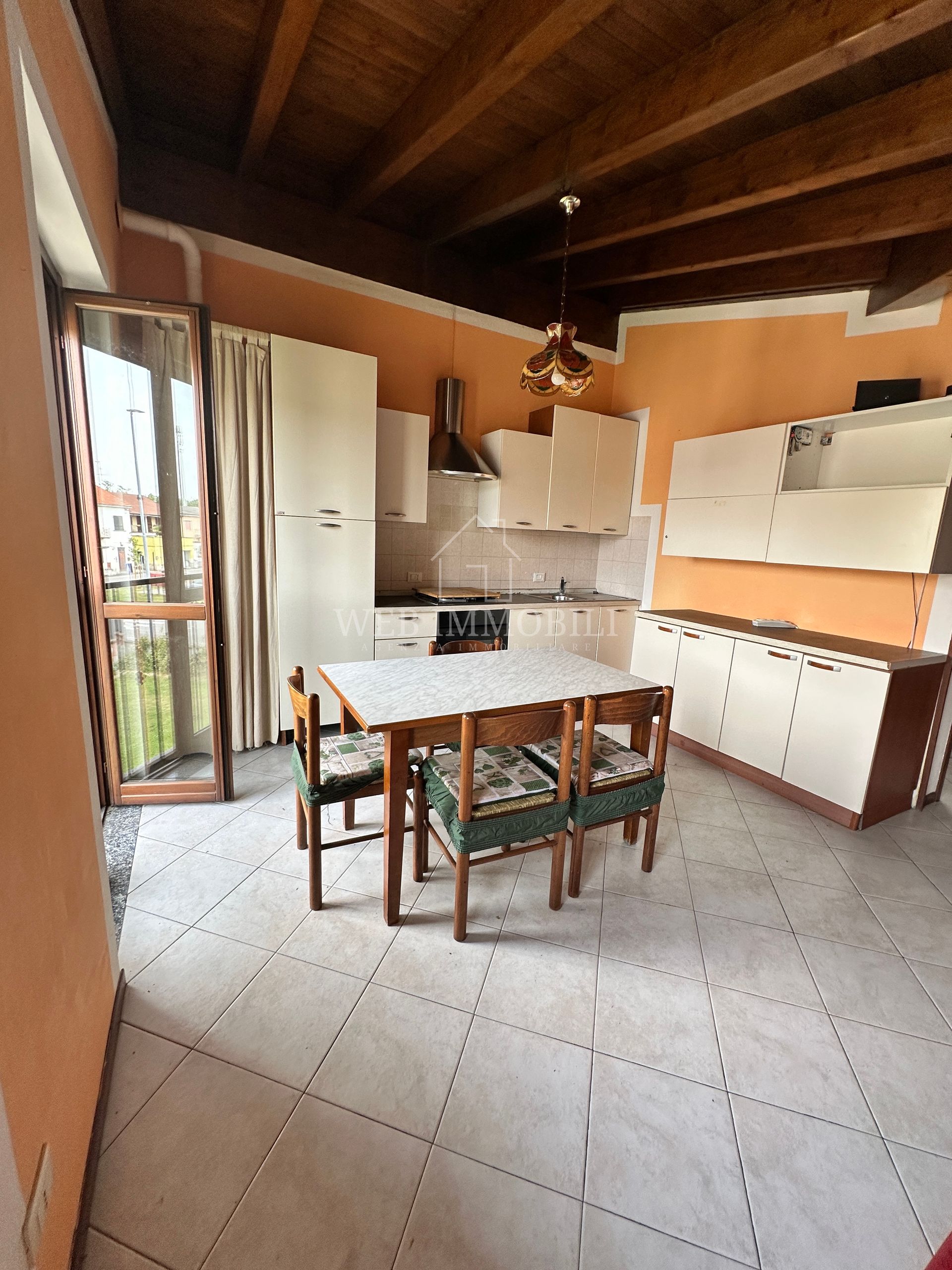 Cucina con tavolo da pranzo, mobili bianchi, pareti arancioni e accesso al balcone.