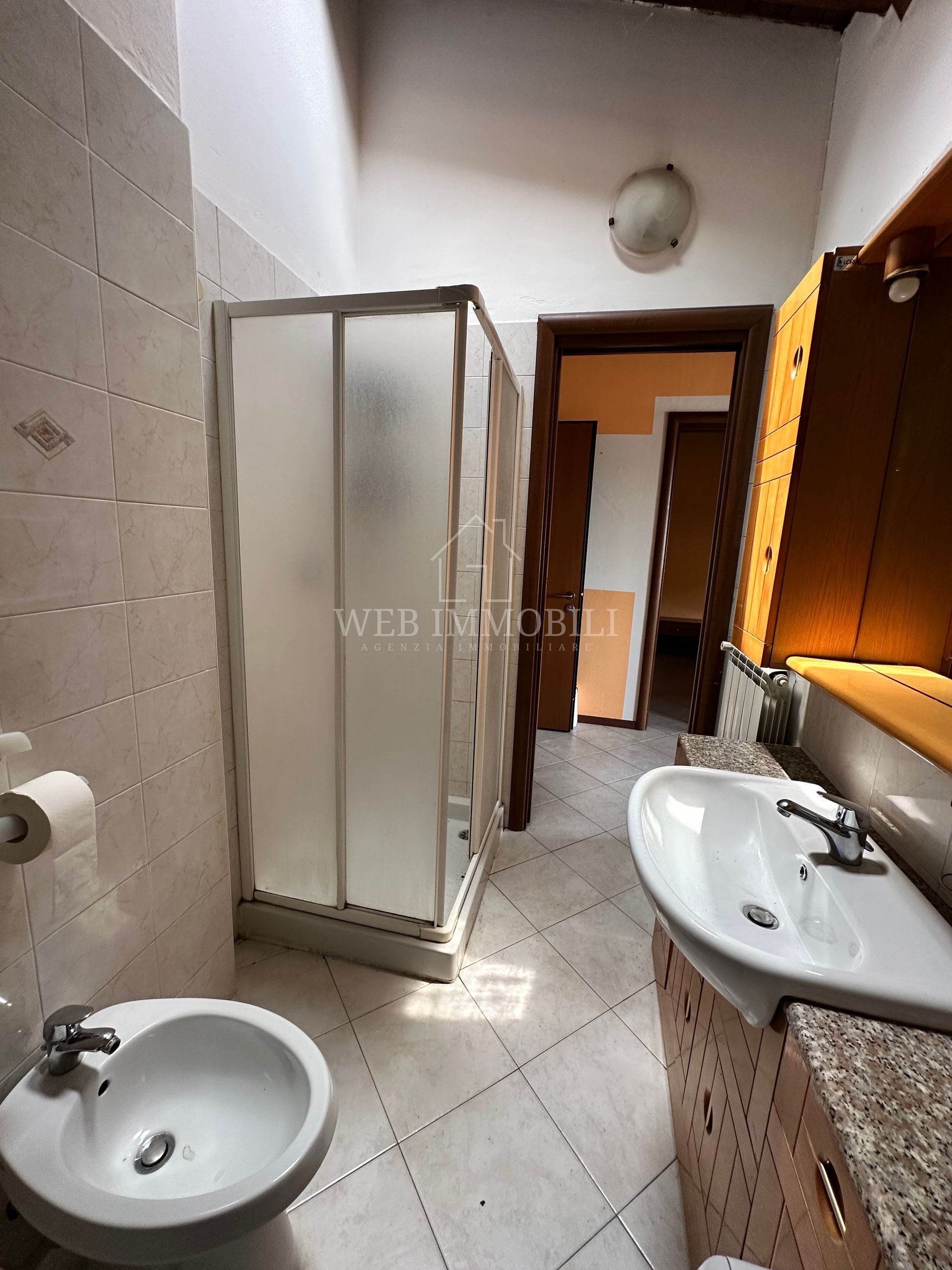 Bagno con doccia, lavandino e bidet; pavimento piastrellato e pareti di colore chiaro.