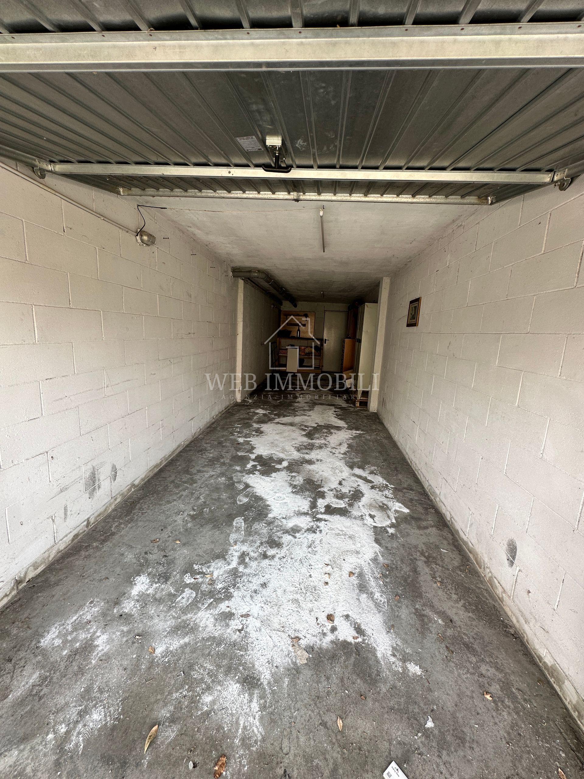 Garage vuoto e stretto con pavimento in cemento, pareti bianche e illuminazione dall'alto.