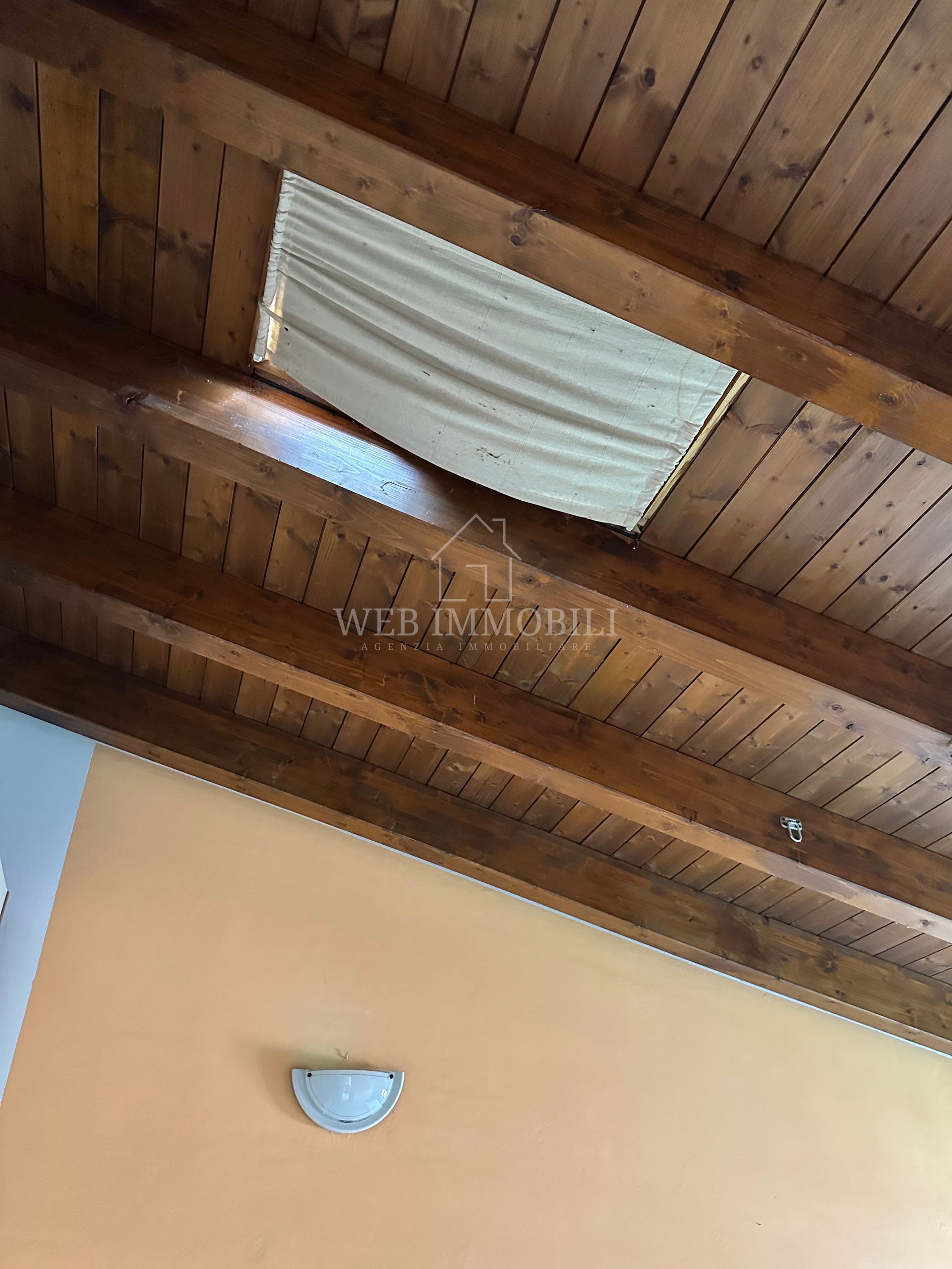 Soffitto in legno con un rettangolo di colore chiaro e una parete arancione con una lampada da parete.
