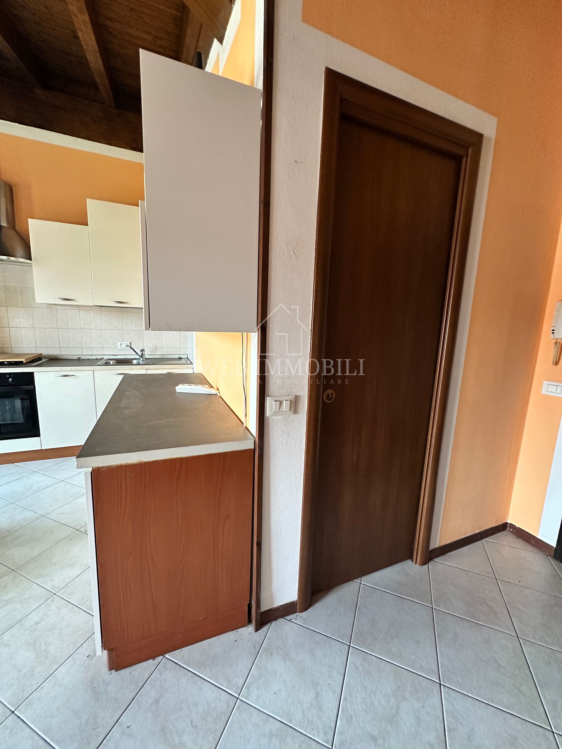 Interno della cucina con mobili, piano di lavoro e una porta di legno chiusa.