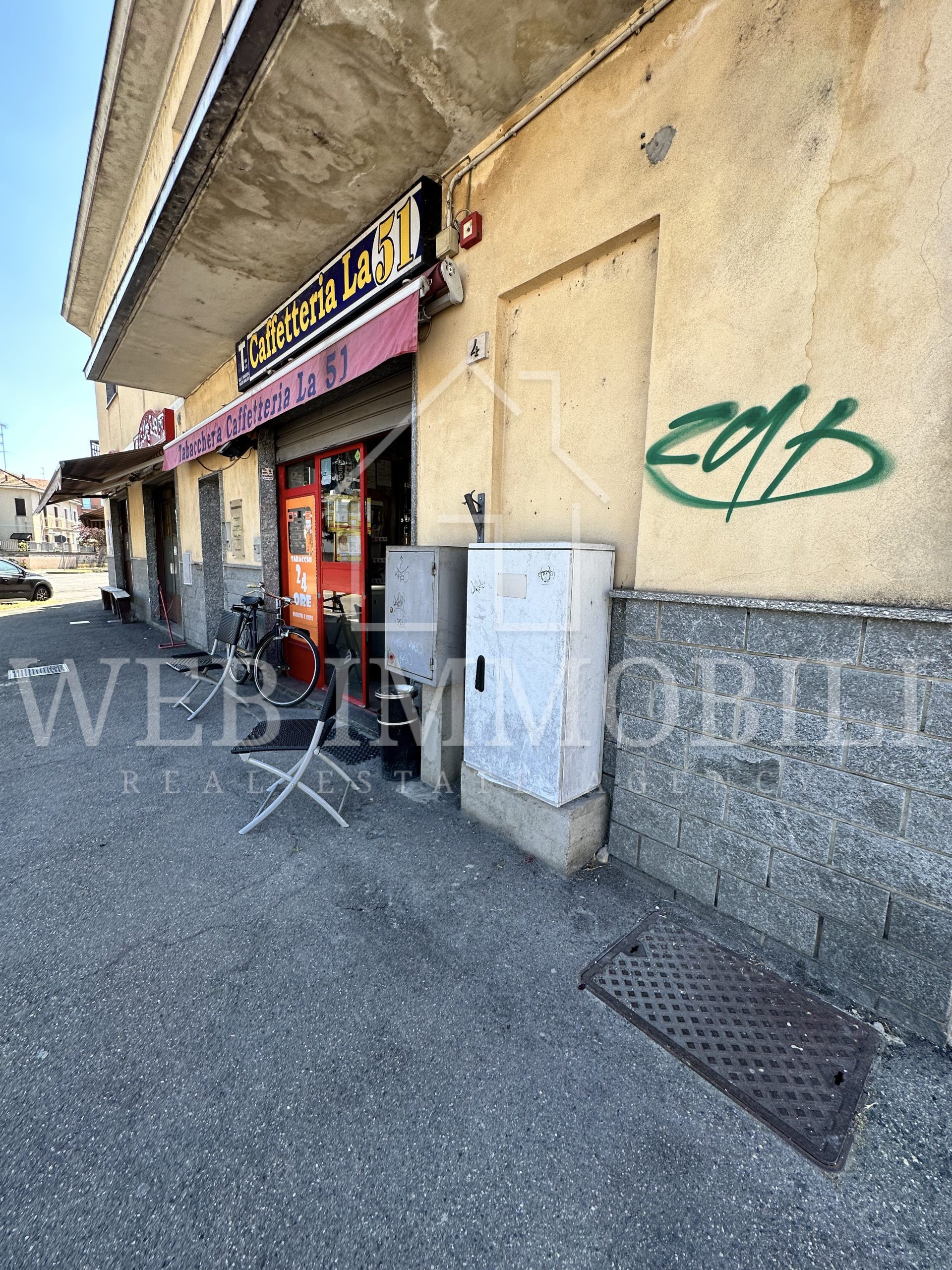 Esterno di un negozio con una tenda rossa, un marciapiede e graffiti su un edificio color marrone chiaro.