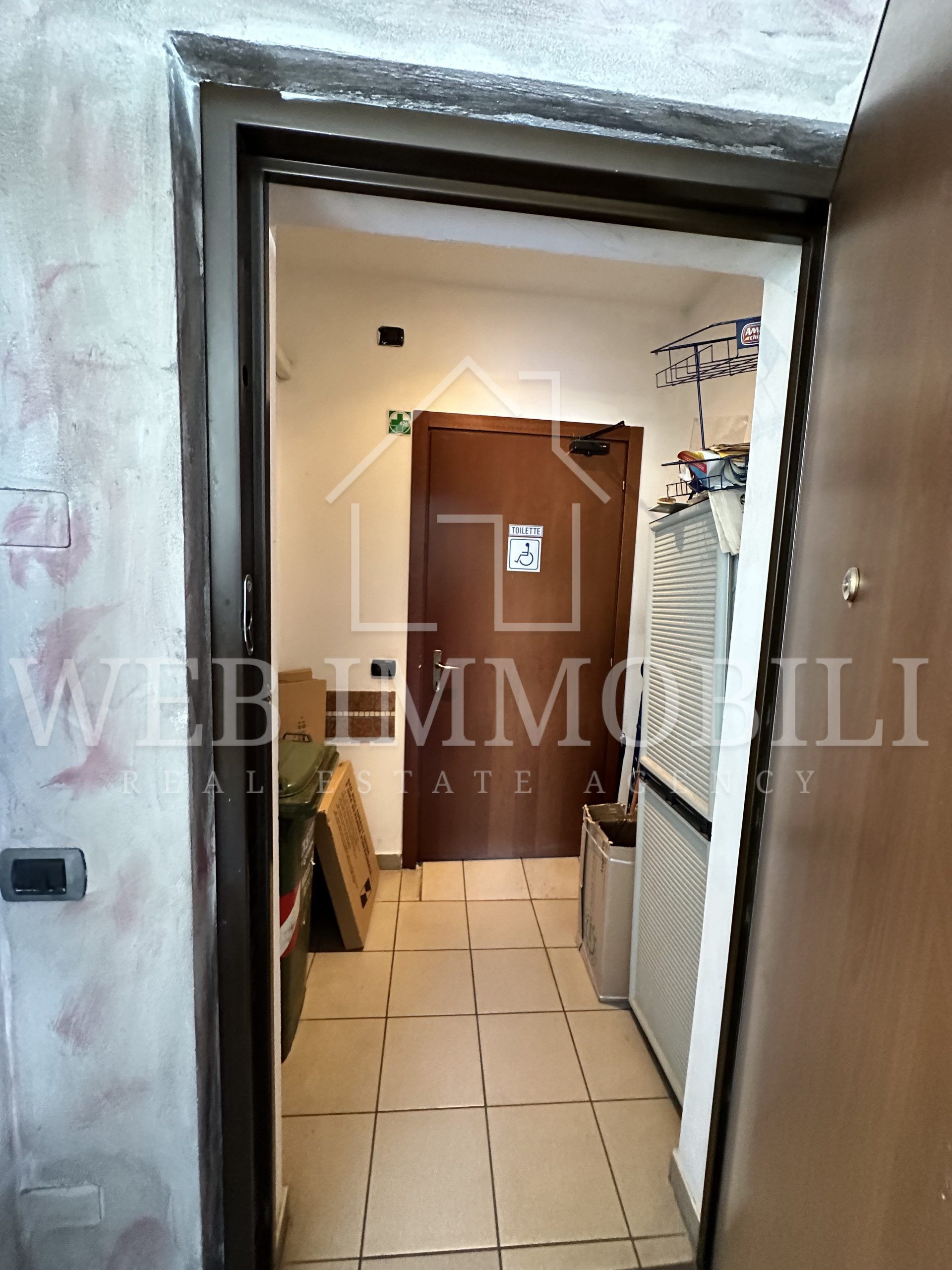 Un ingresso con una porta aperta che conduce a un corridoio con una porta in fondo.