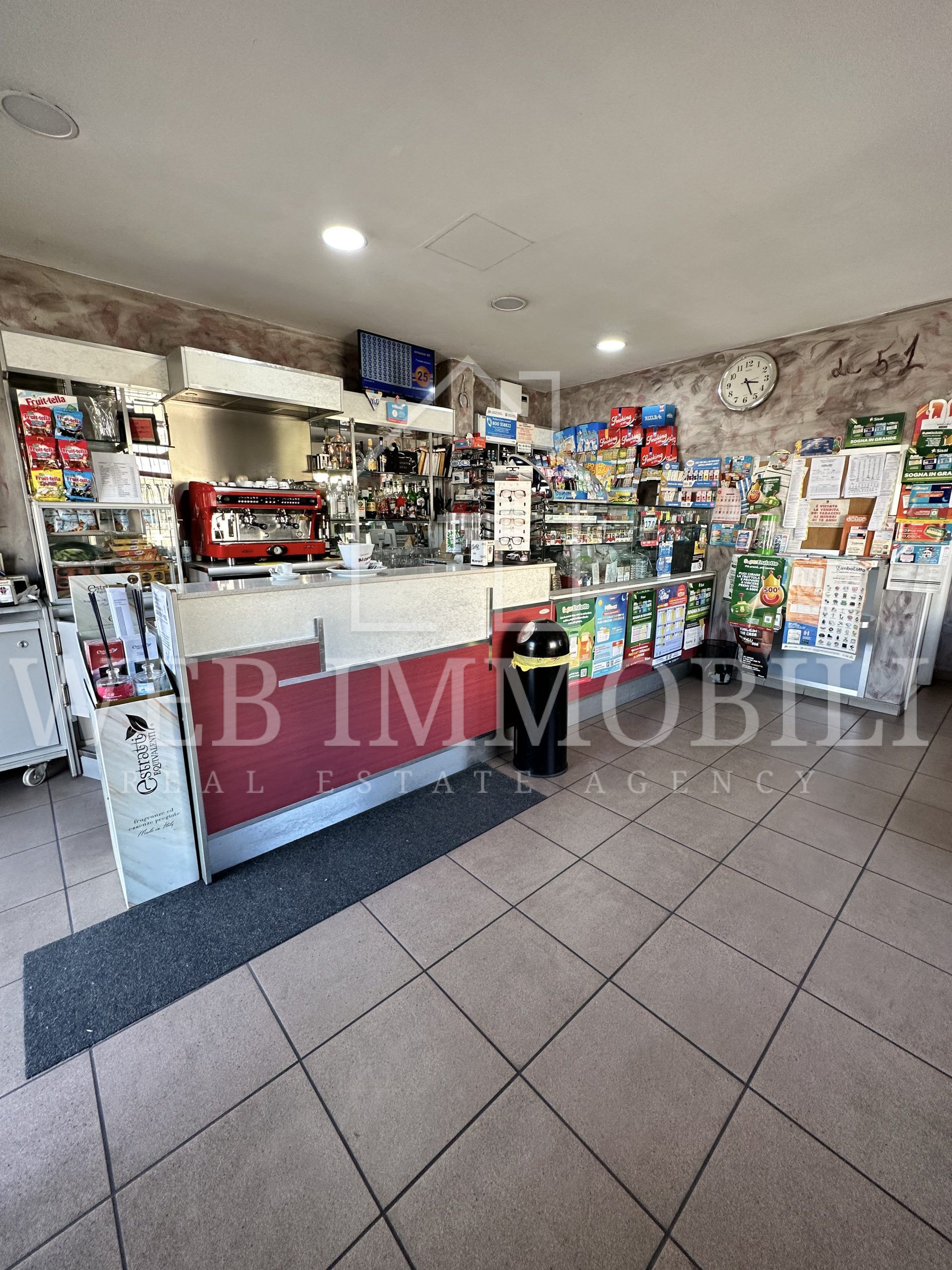 Interno di un negozio con scaffali, bancone e prodotti. È visibile una macchina per il caffè.