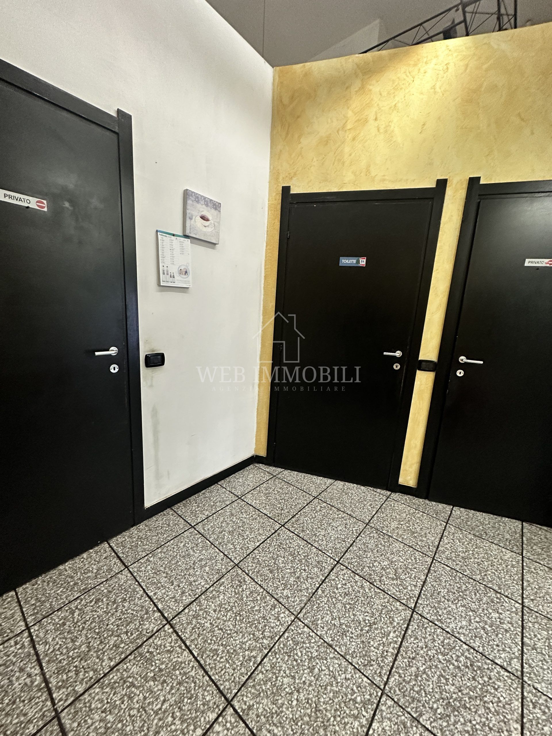 Corridoio con tre porte nere, pavimento decorato e una parete dipinta di bianco e oro.