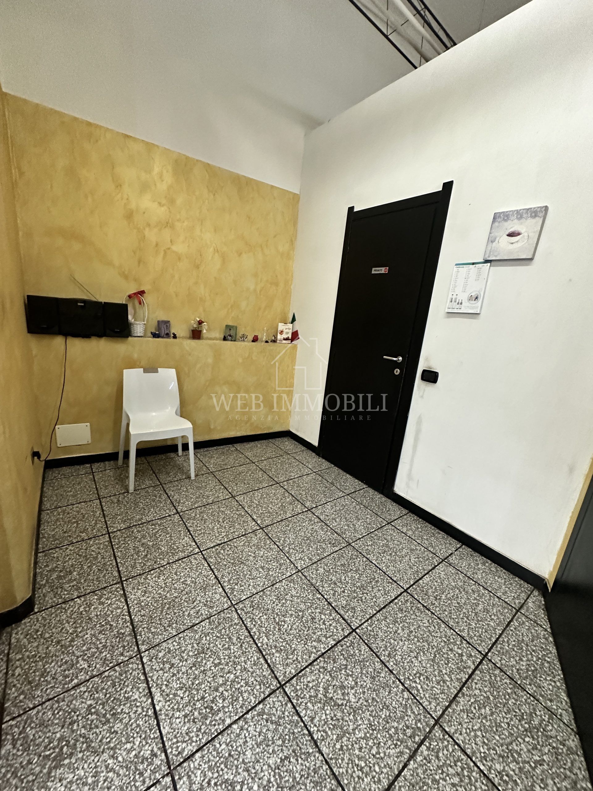 Piccola stanza con pavimento in piastrelle screziate, porta nera, sedia bianca e pareti gialle e bianche.