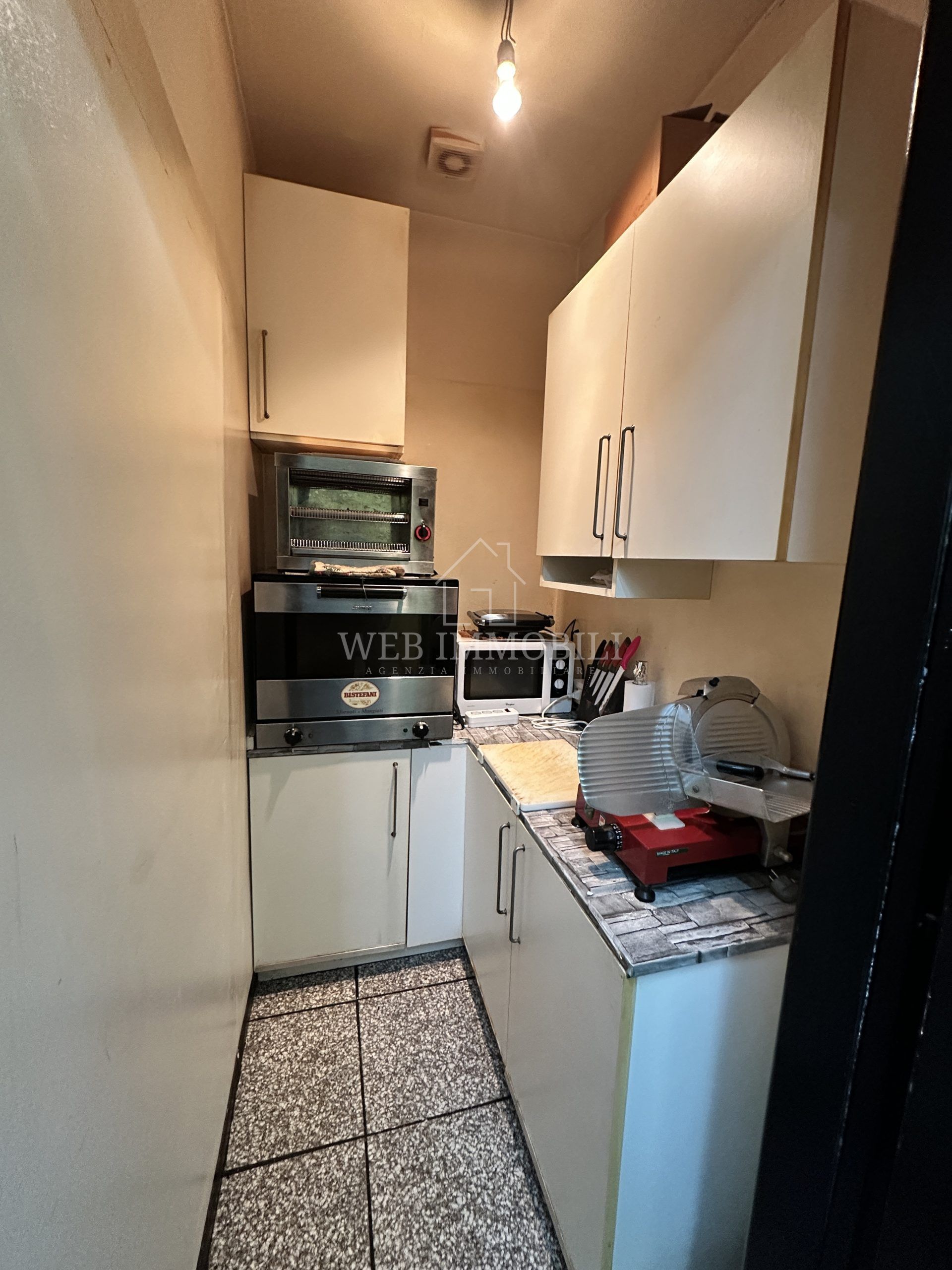 Piccola cucina con mobili color crema, elettrodomestici e piano di lavoro.