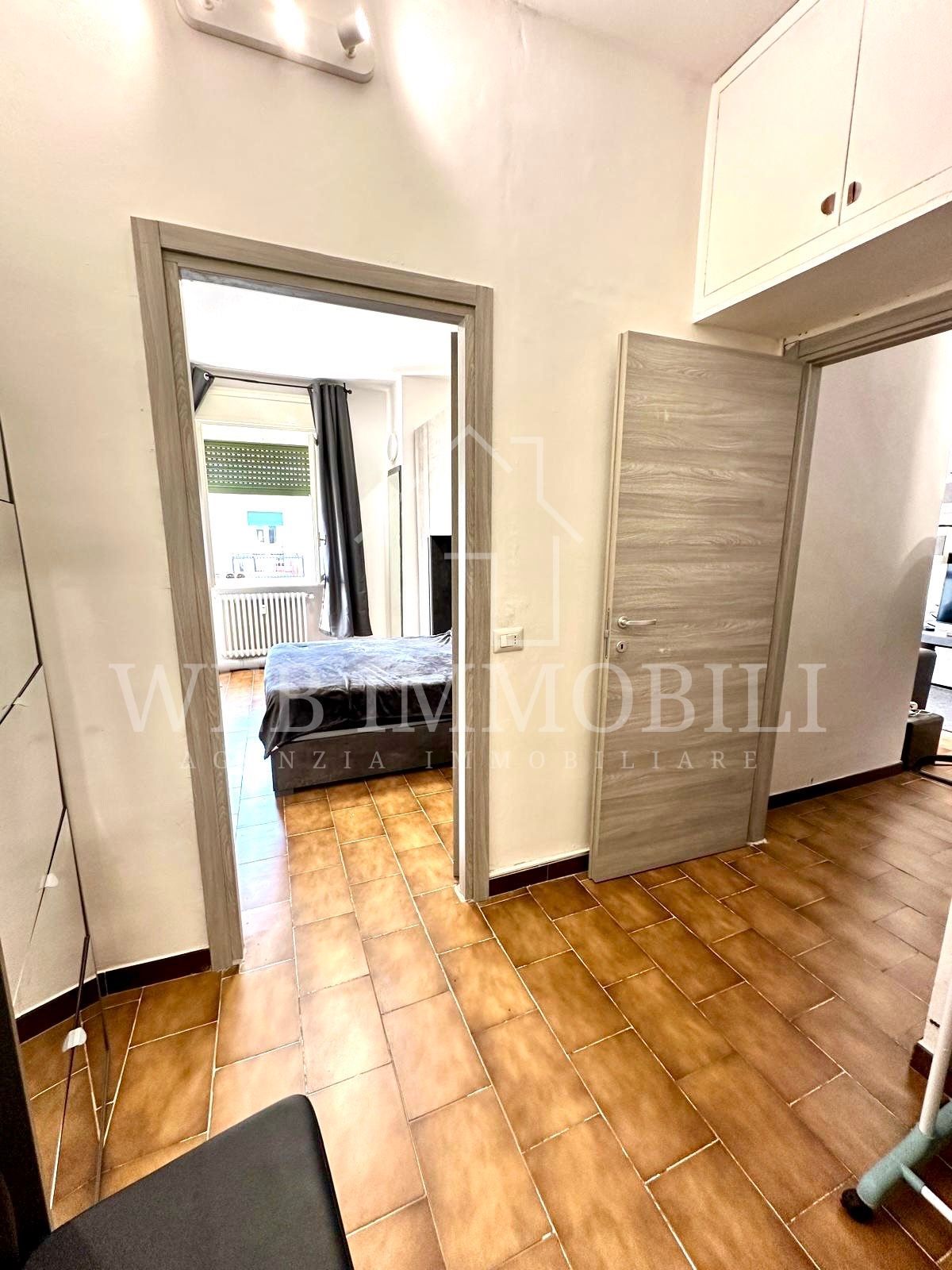 Corridoio con porte aperte su una camera da letto e un'altra stanza. Pavimento in piastrelle marroni, porte effetto legno e armadi a muro.