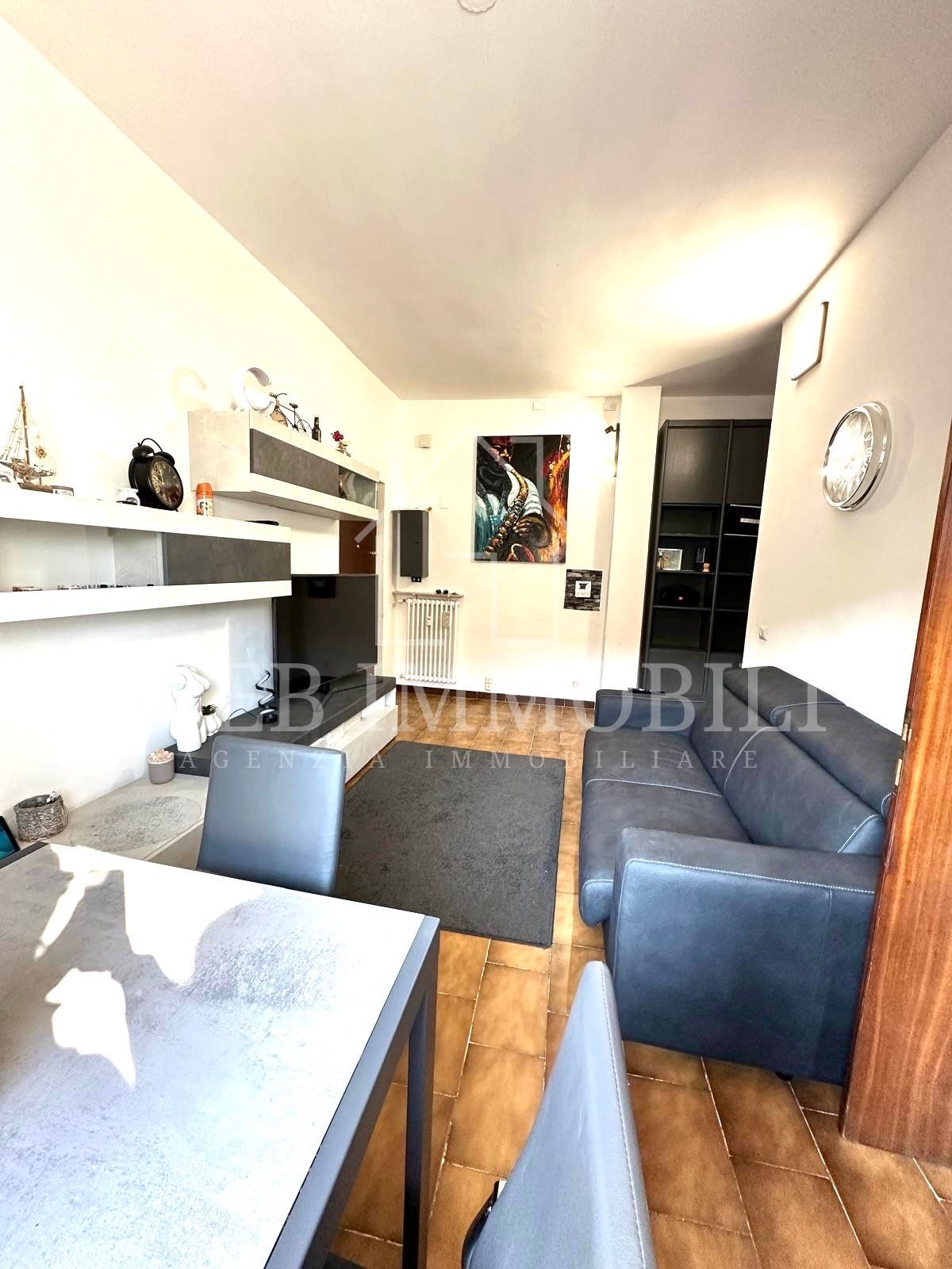 Piccolo soggiorno con mobili grigi, pavimenti in legno e un tavolo.