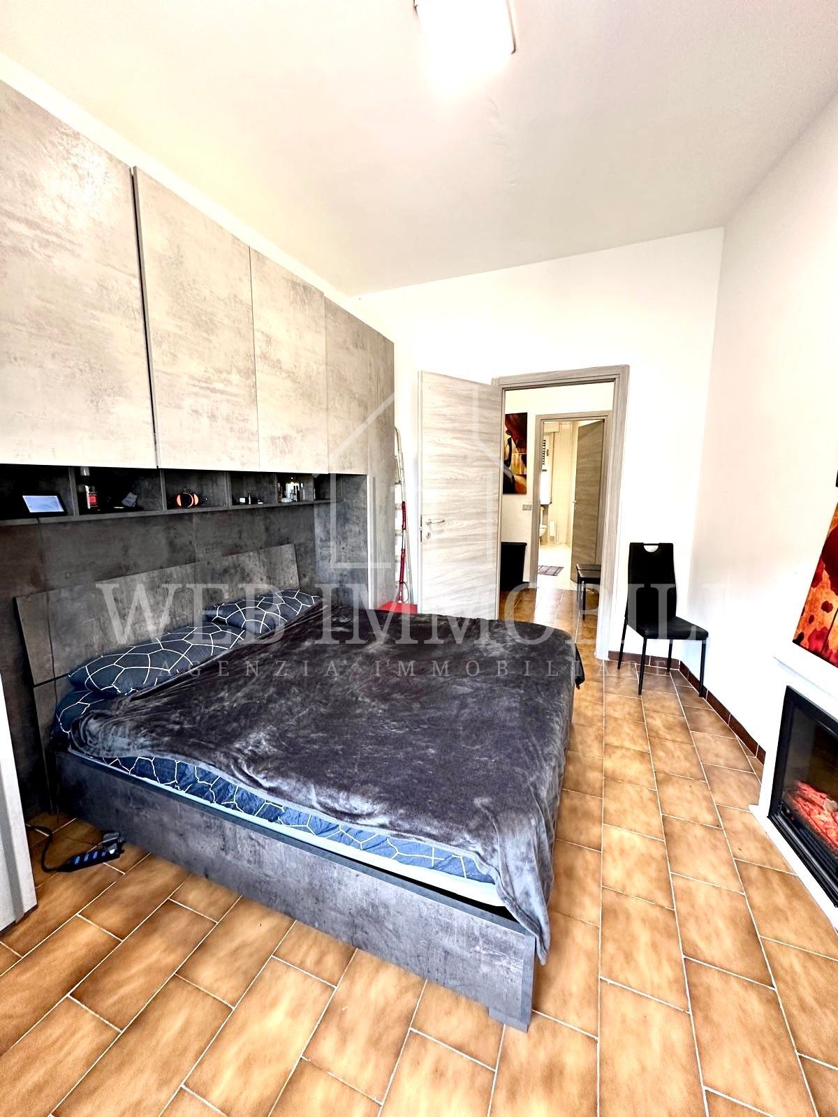 Camera da letto con letto grigio, parete in pietra e porta che conduce al bagno. Pavimenti in legno e camino.