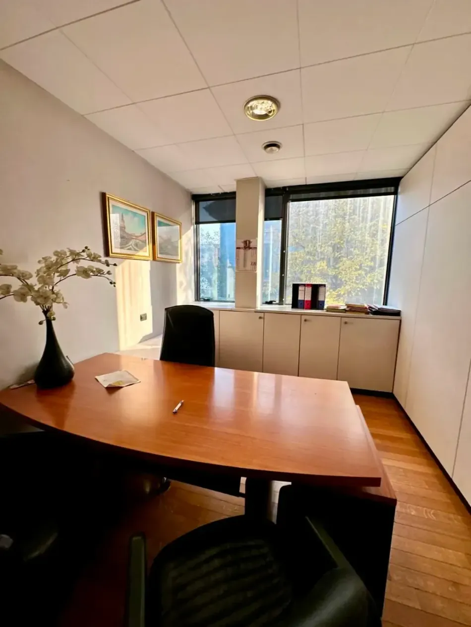 Ufficio con scrivania, sedie, finestra, armadi e opere d'arte. Tonalità calde del legno e pareti neutre.