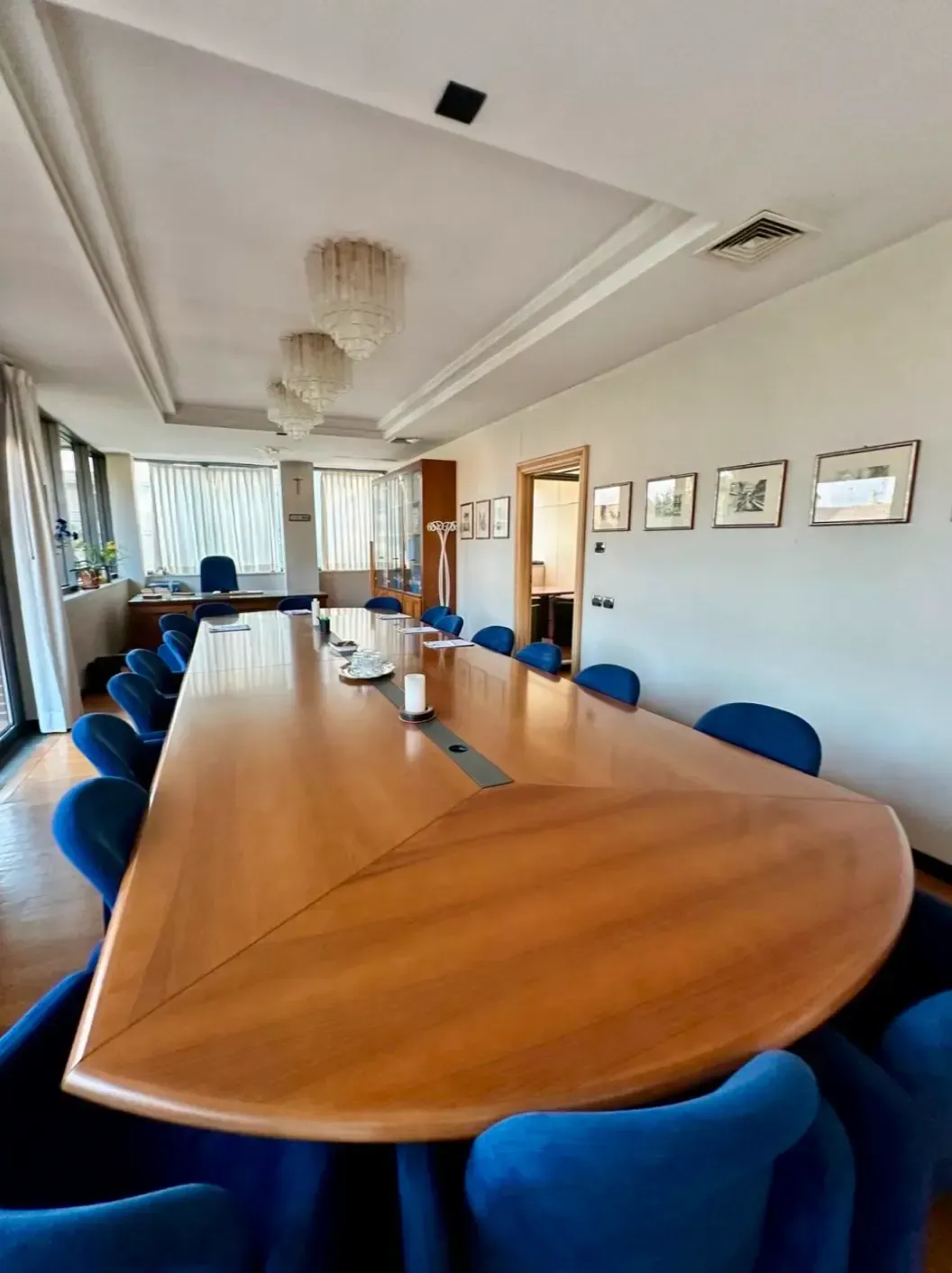 Una sala conferenze con un lungo tavolo di legno e sedie blu. Quadri appesi alle pareti.