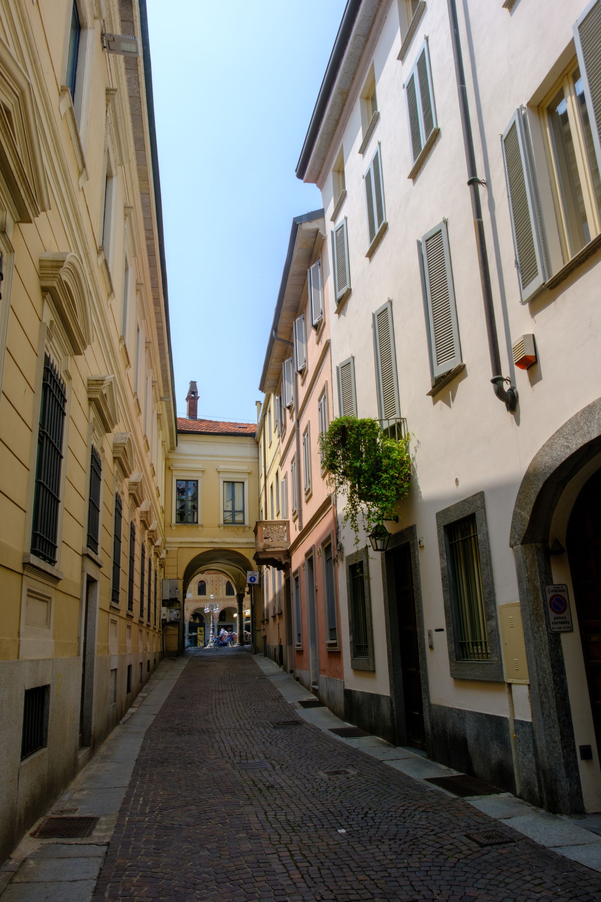 Strada acciottolata tra edifici color pastello con ingresso ad arco; luce del sole.