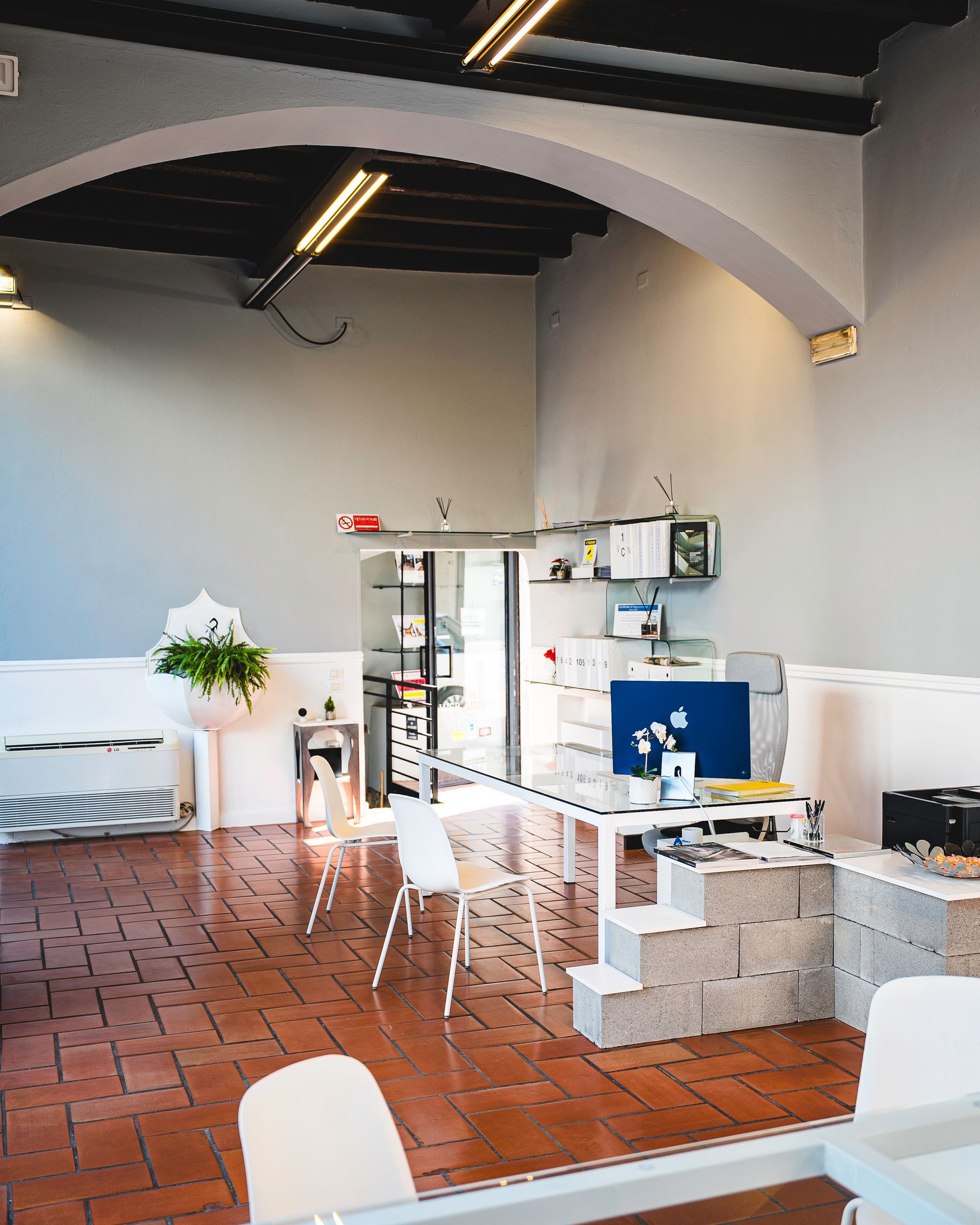 Ufficio moderno con pareti in vetro, scrivania e cortile esterno visibile.