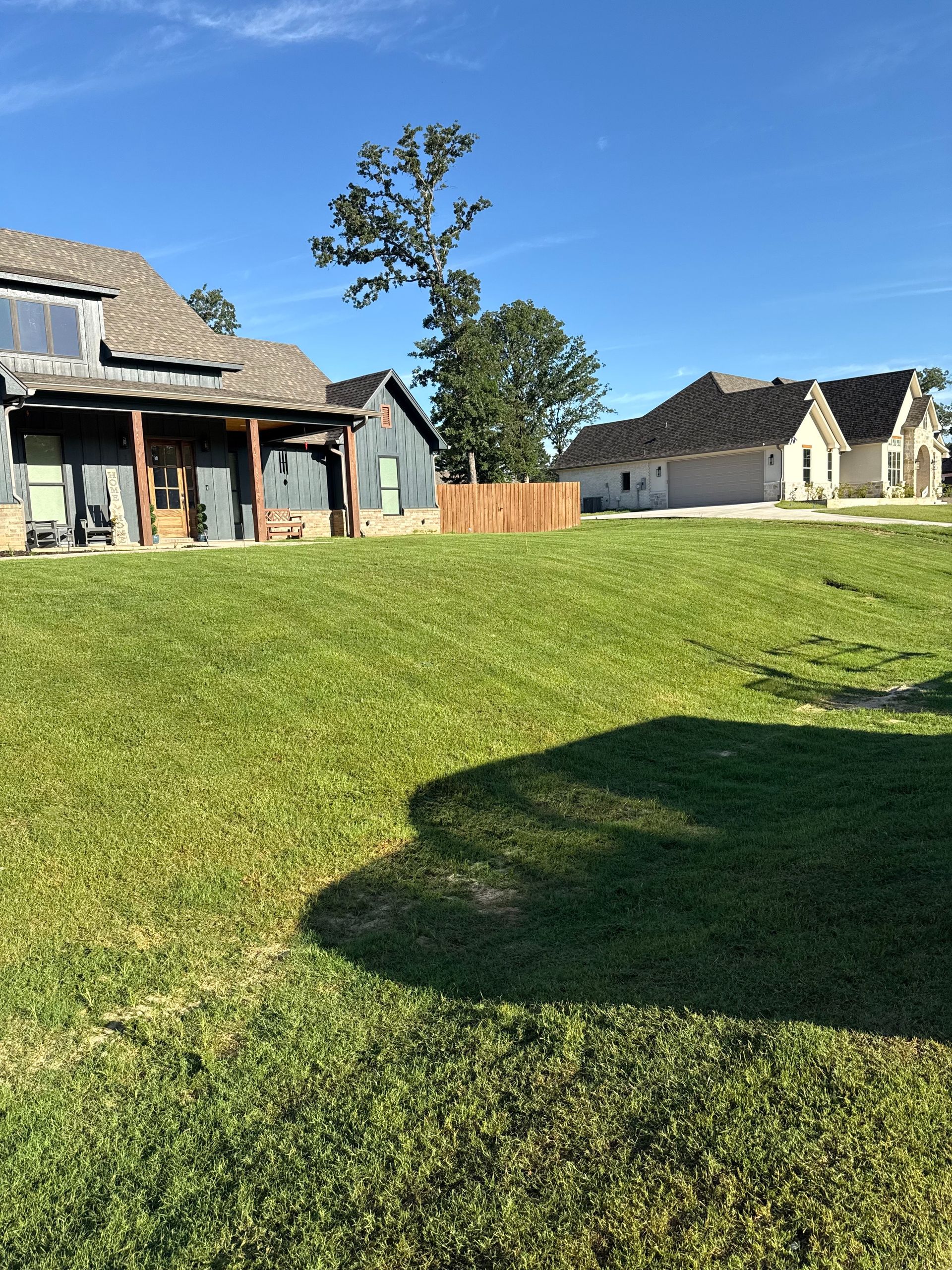 Green lawn with several houses under a blue sky. One house is shaded and has wooden beams.