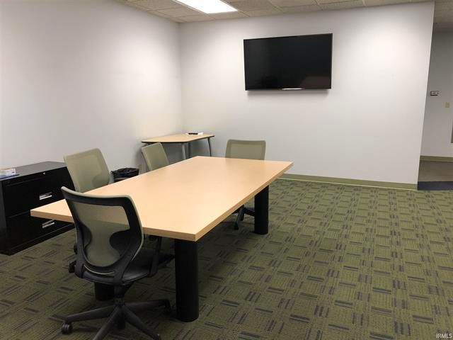 A conference room with a table and chairs and a flat screen tv on the wall.