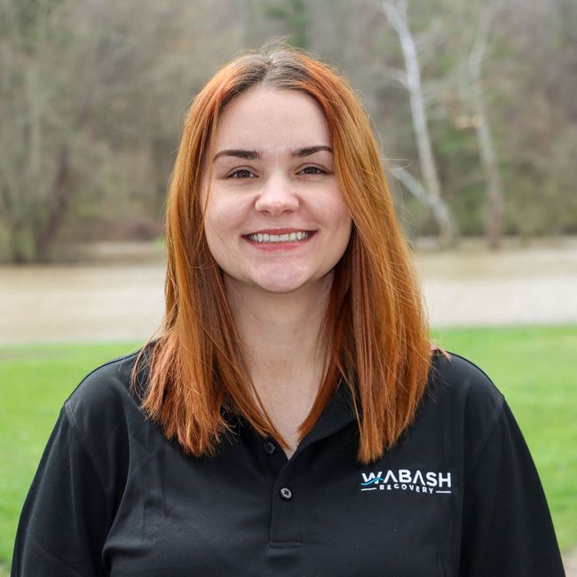 A woman with red hair is wearing a black shirt and smiling.