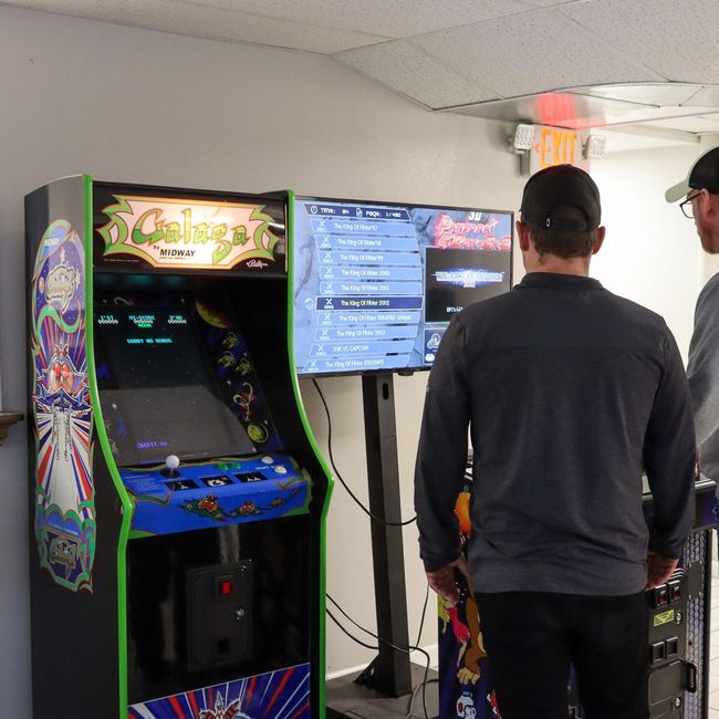 Two men standing in front of an arcade machine that says genius