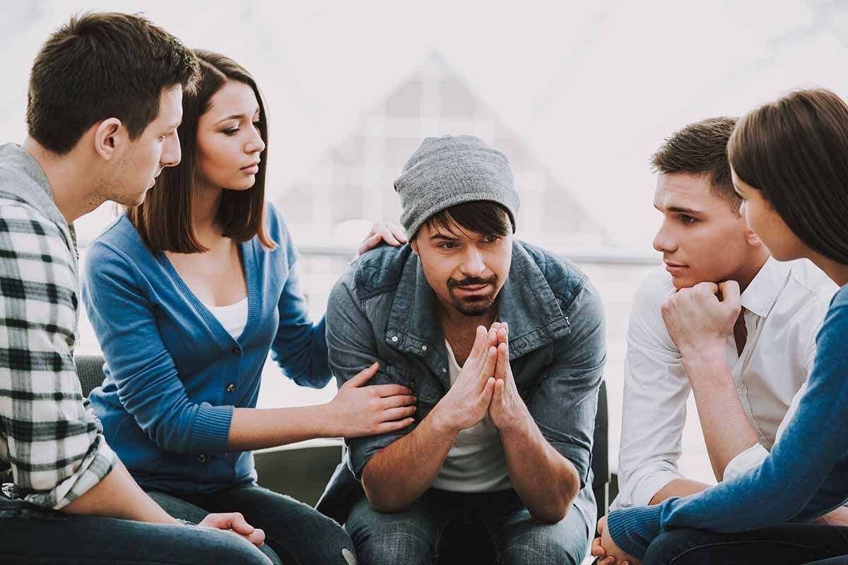 A group of young people are sitting around a man in a chair.