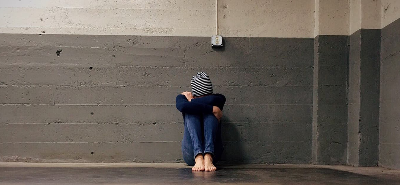 A person is sitting on the floor with their head on the wall.