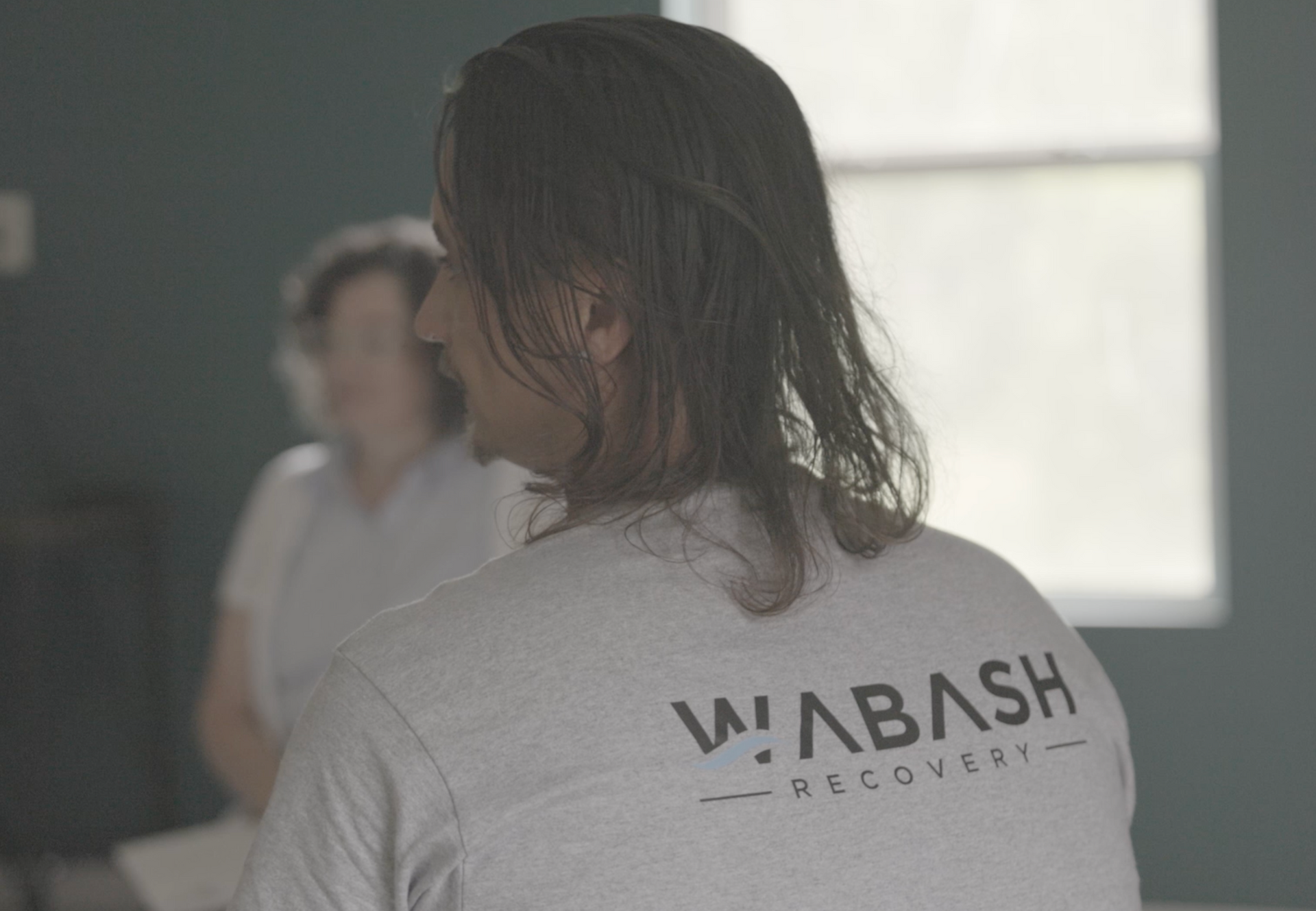 A man with long hair is wearing a wabash recovery shirt