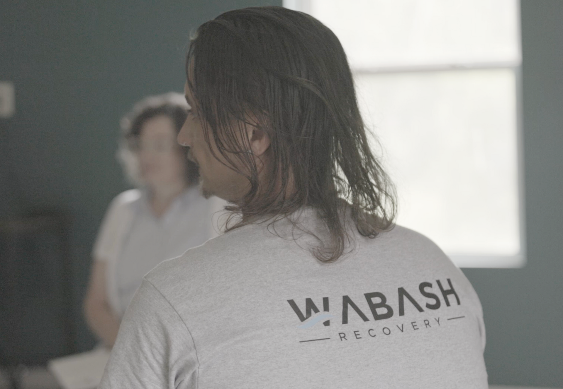 A man with long hair is wearing a wabash recovery shirt