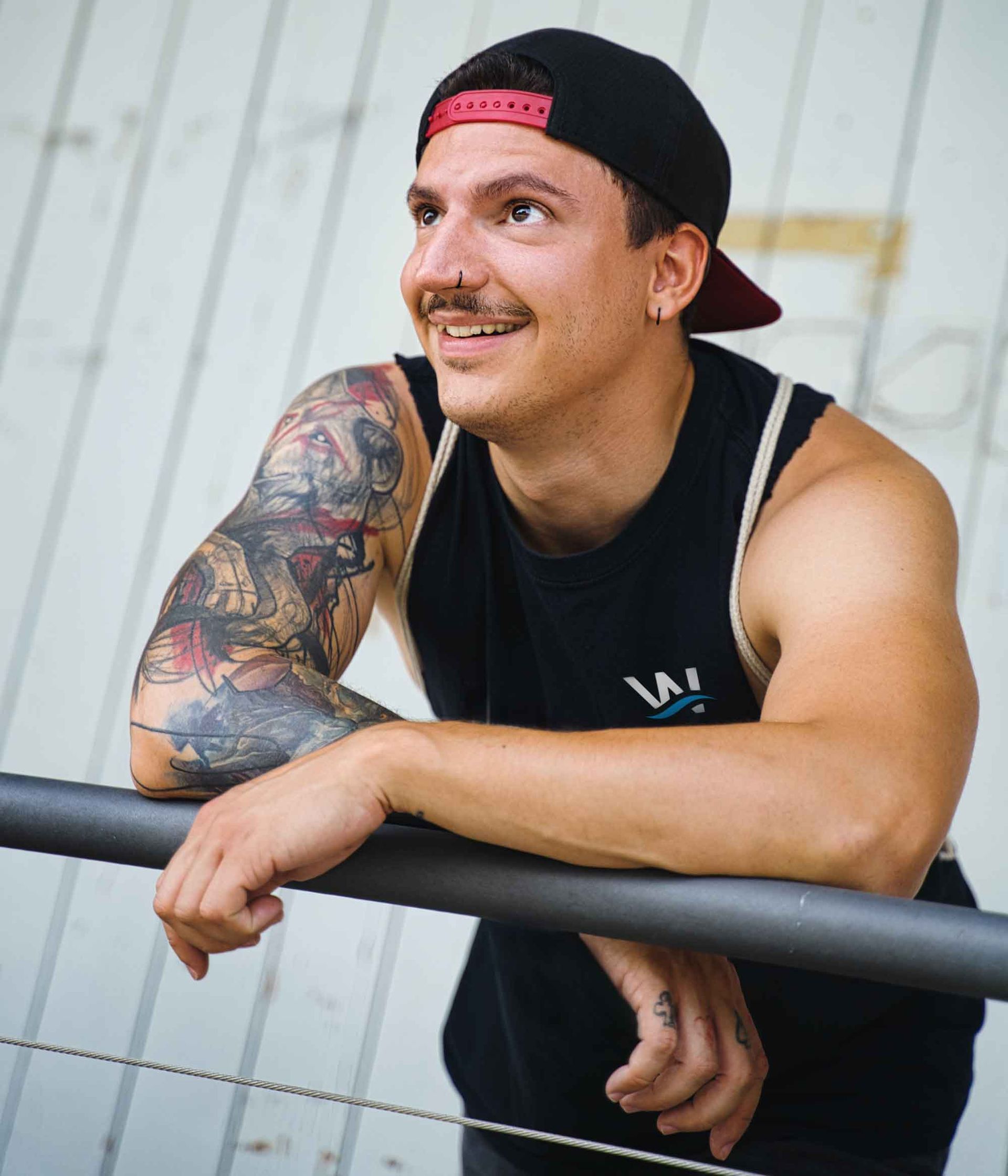 A man with a tattoo on his arm is leaning on a railing.