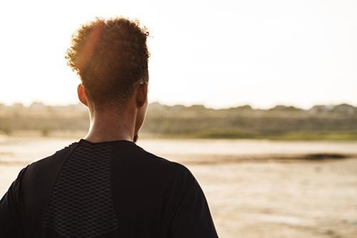 A man is standing on a beach looking at the water.