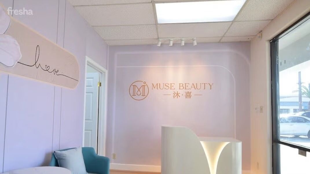 Reception area of Muse Beauty with a white curved desk, logo, and light purple walls.