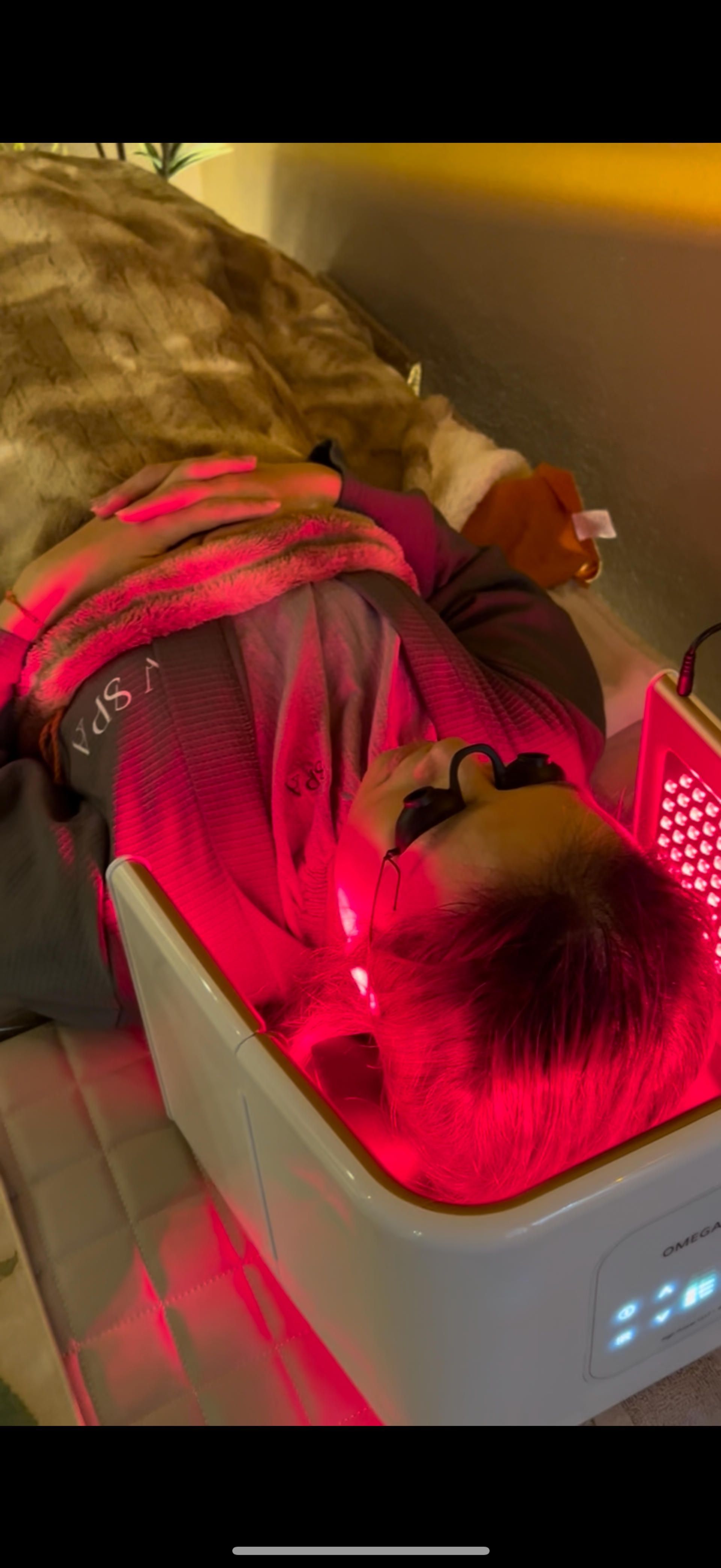 A person lying under a red light therapy device; wearing safety glasses.