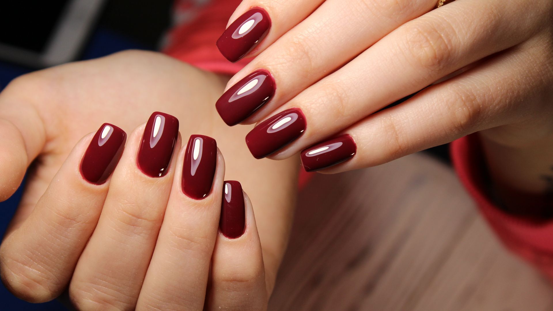 Hands with polished, dark red, oval-shaped nails.