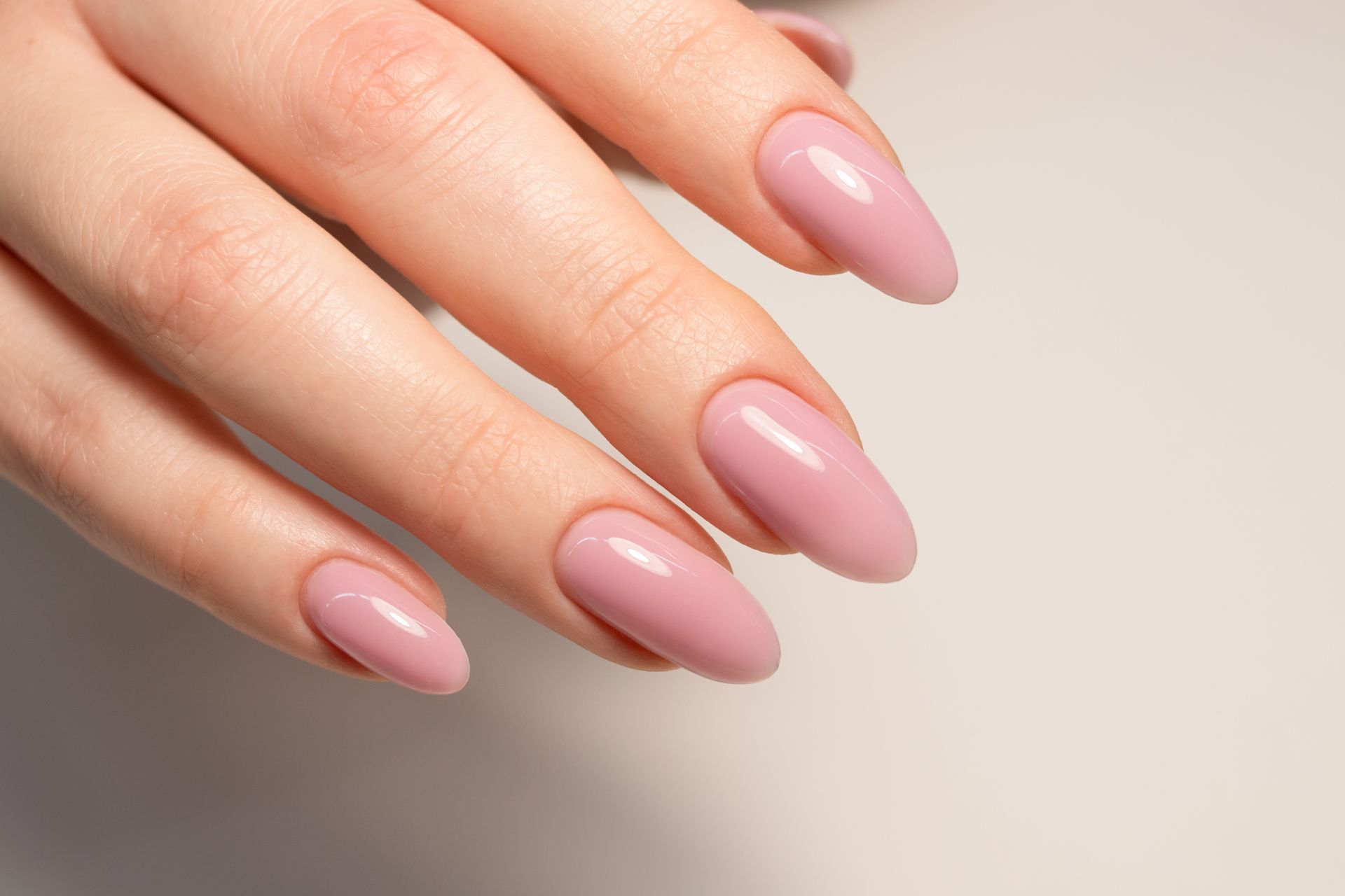 Hand with almond-shaped nails painted a pale pink, resting on a white surface.