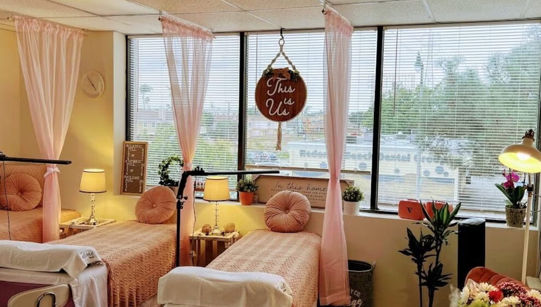 Pink-themed spa with three beds, sheer curtains, lamps, and a window overlooking an outdoor view.