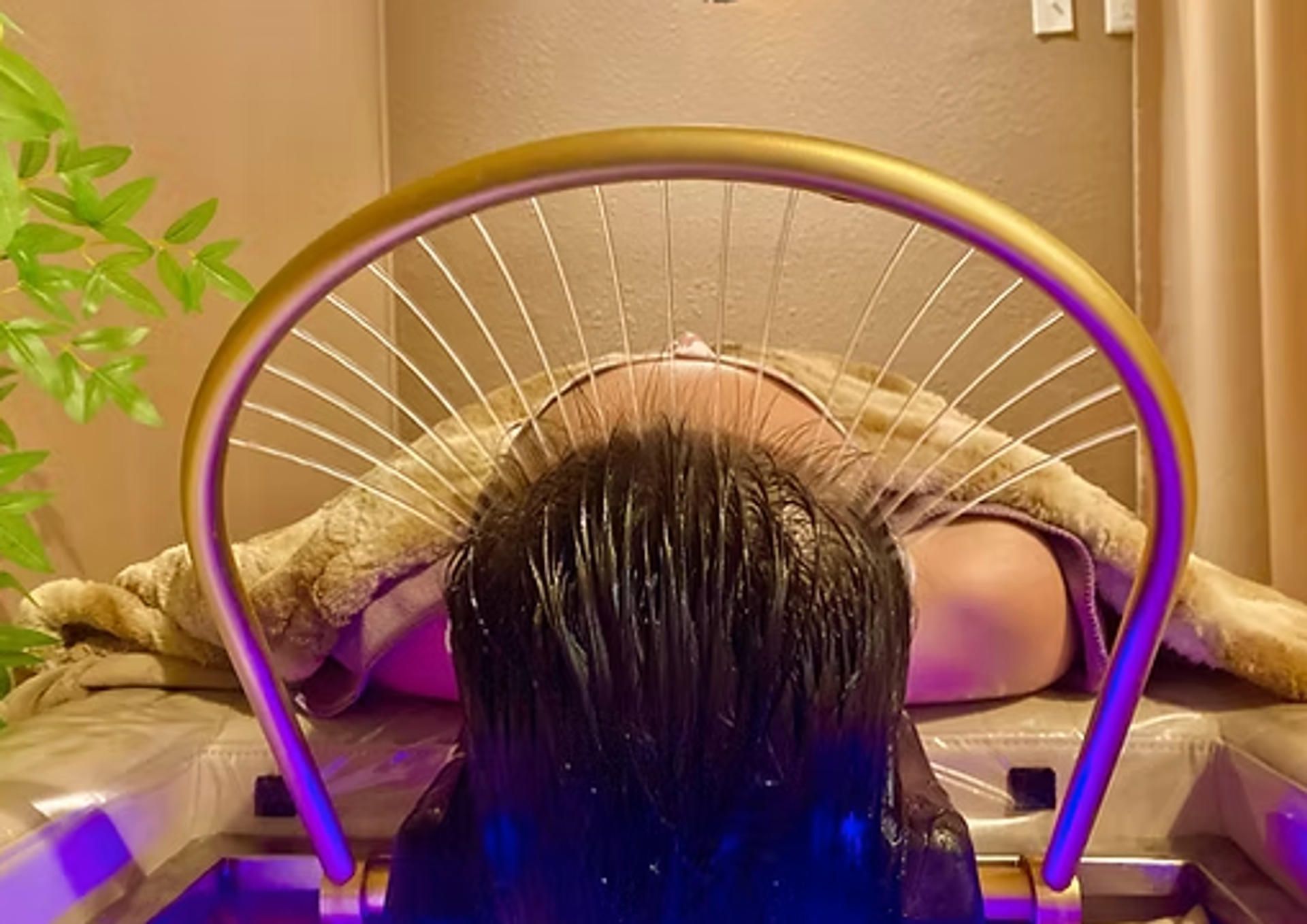 Person undergoing a hair spa treatment, with water cascading over their head under a gold arc.