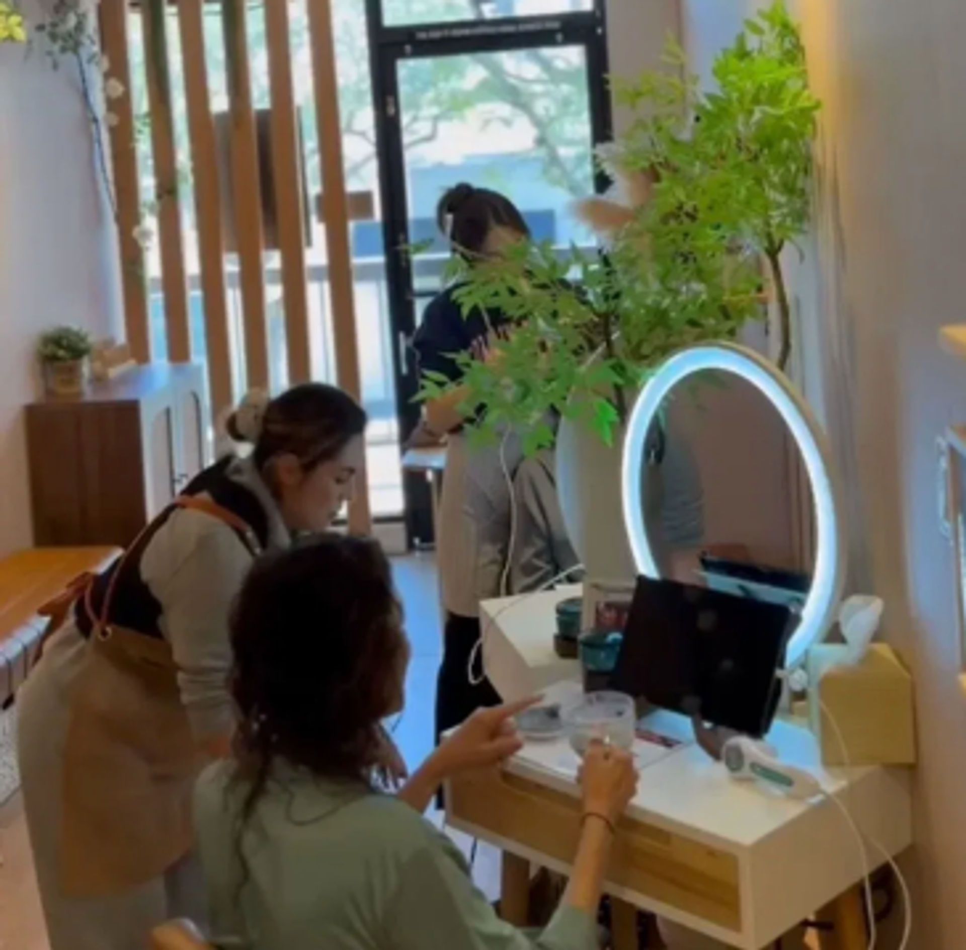 Three people in a beauty room. One at vanity table, one assisting, and another standing behind them.