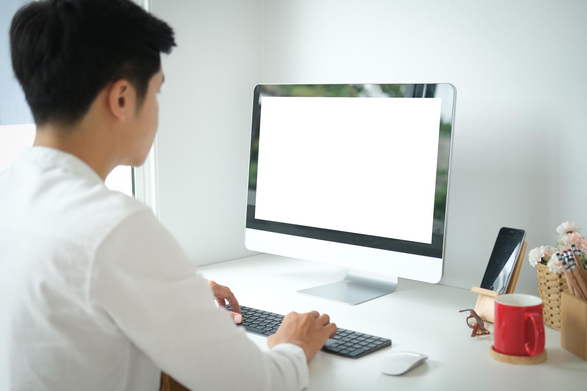 Person typing on keyboard, seated at a desk with a computer monitor, phone, and mug.
