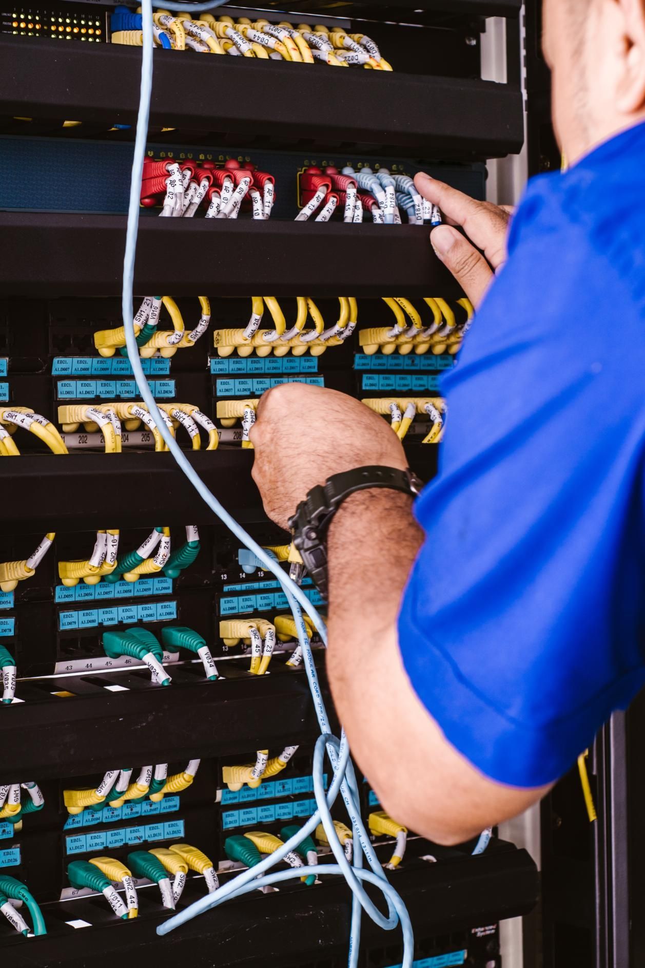 Person in blue shirt working on network cables in a server rack; cables are yellow, blue, and red.