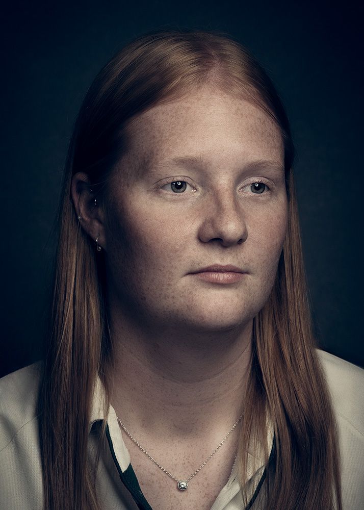 A woman with long red hair is wearing a necklace and earrings in the classic fine art photo portrait.