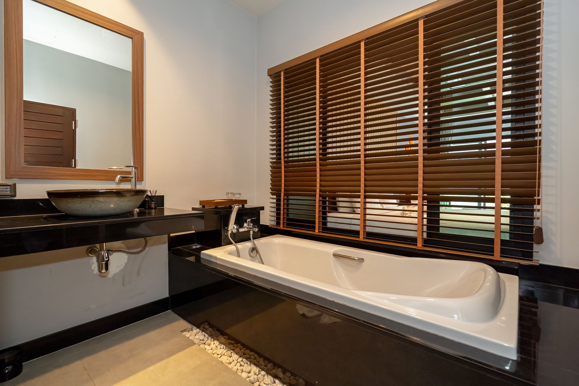 A bathroom with a bathtub , sink , mirror and blinds.