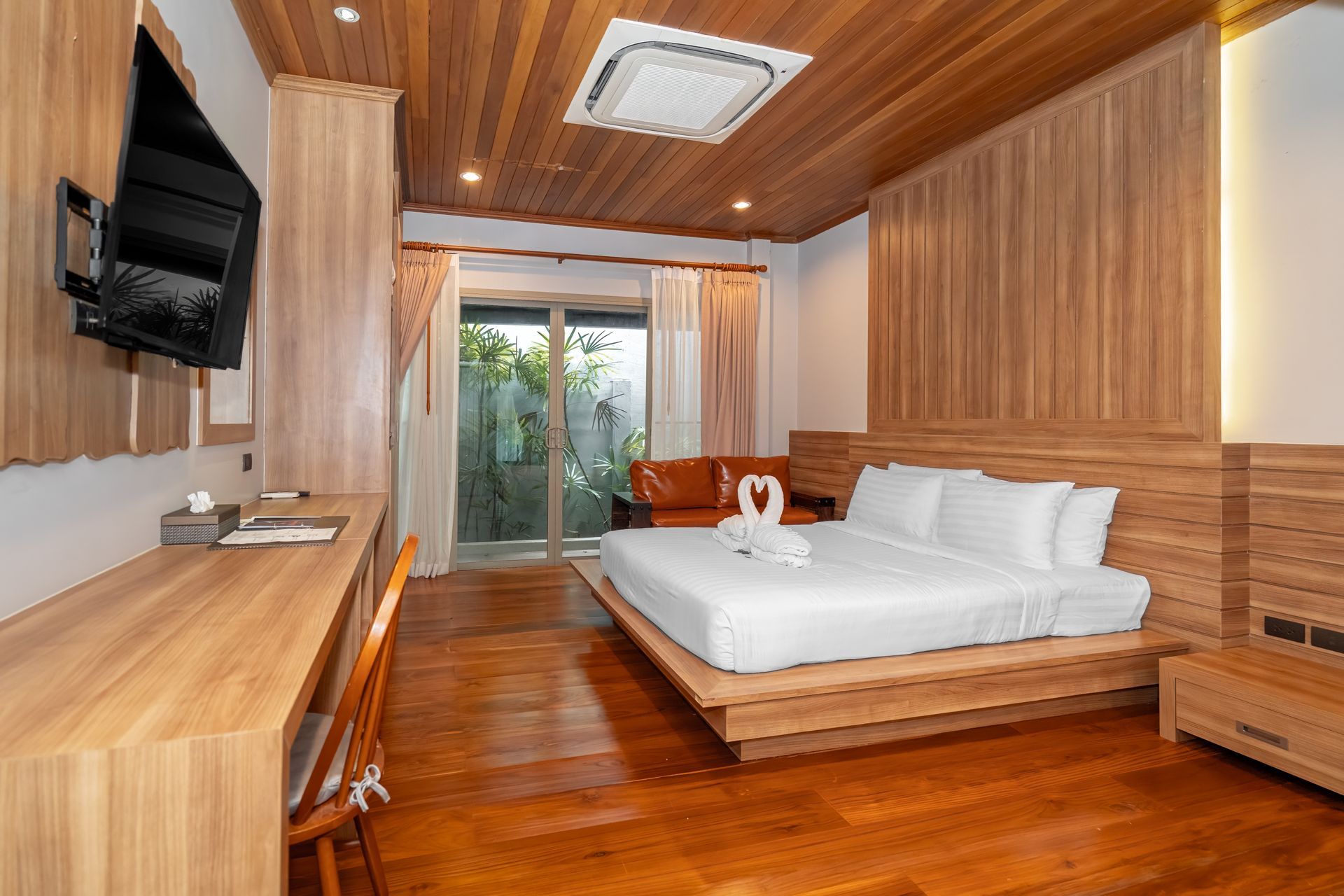 A hotel room with a bed , desk , television and wooden floors.