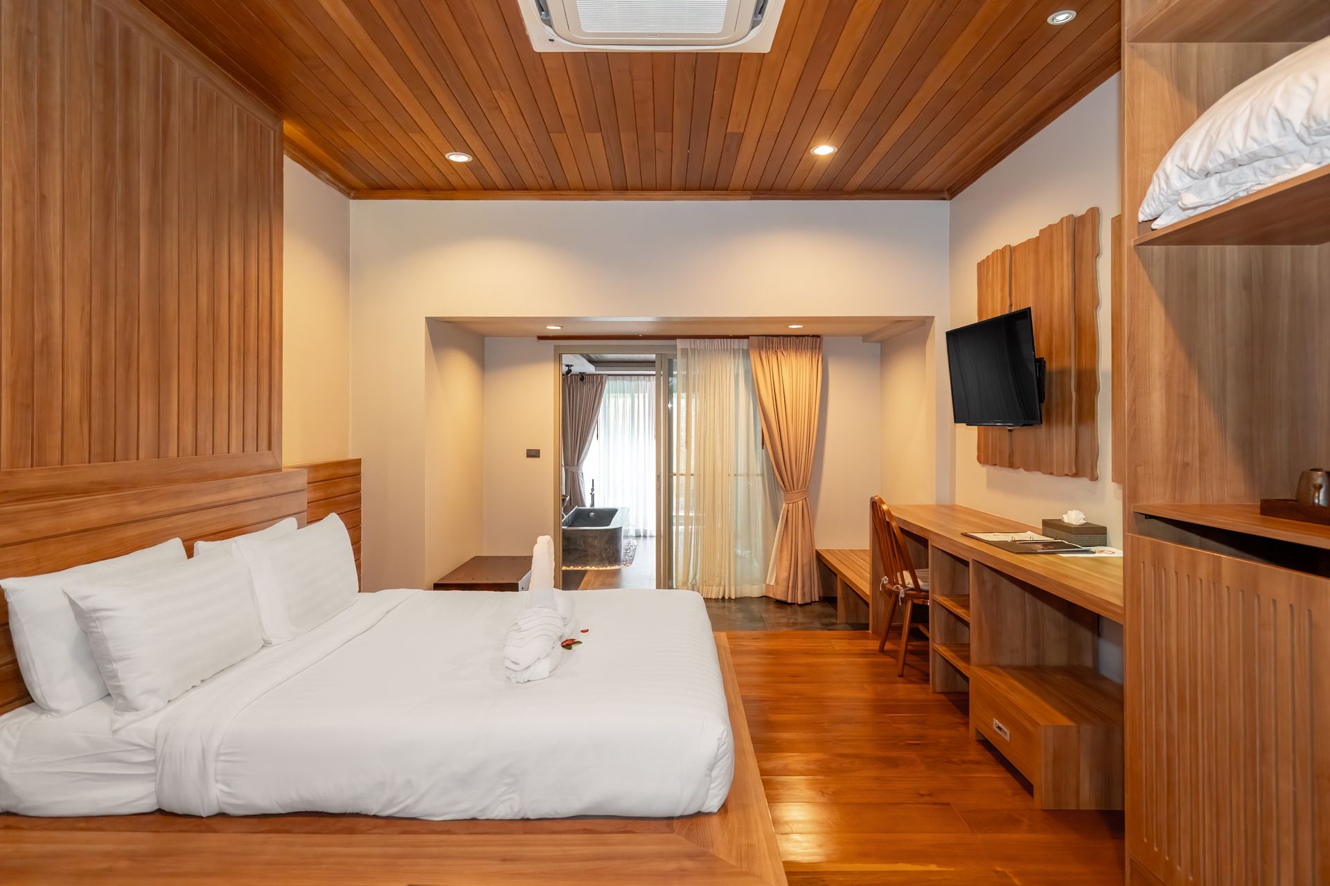 A hotel room with a bed , desk , television and wooden floors.