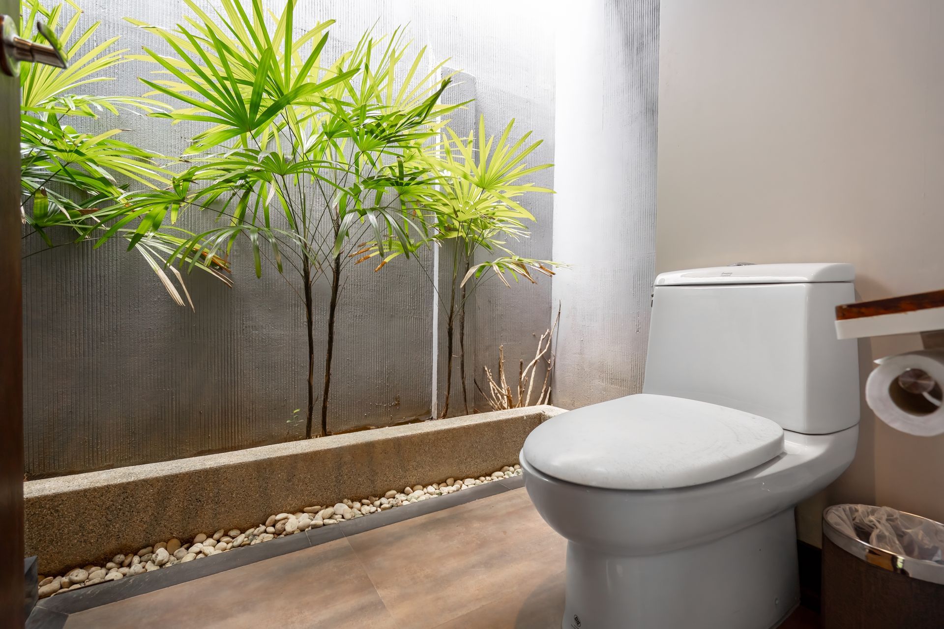 A bathroom with a toilet and a plant in the background.