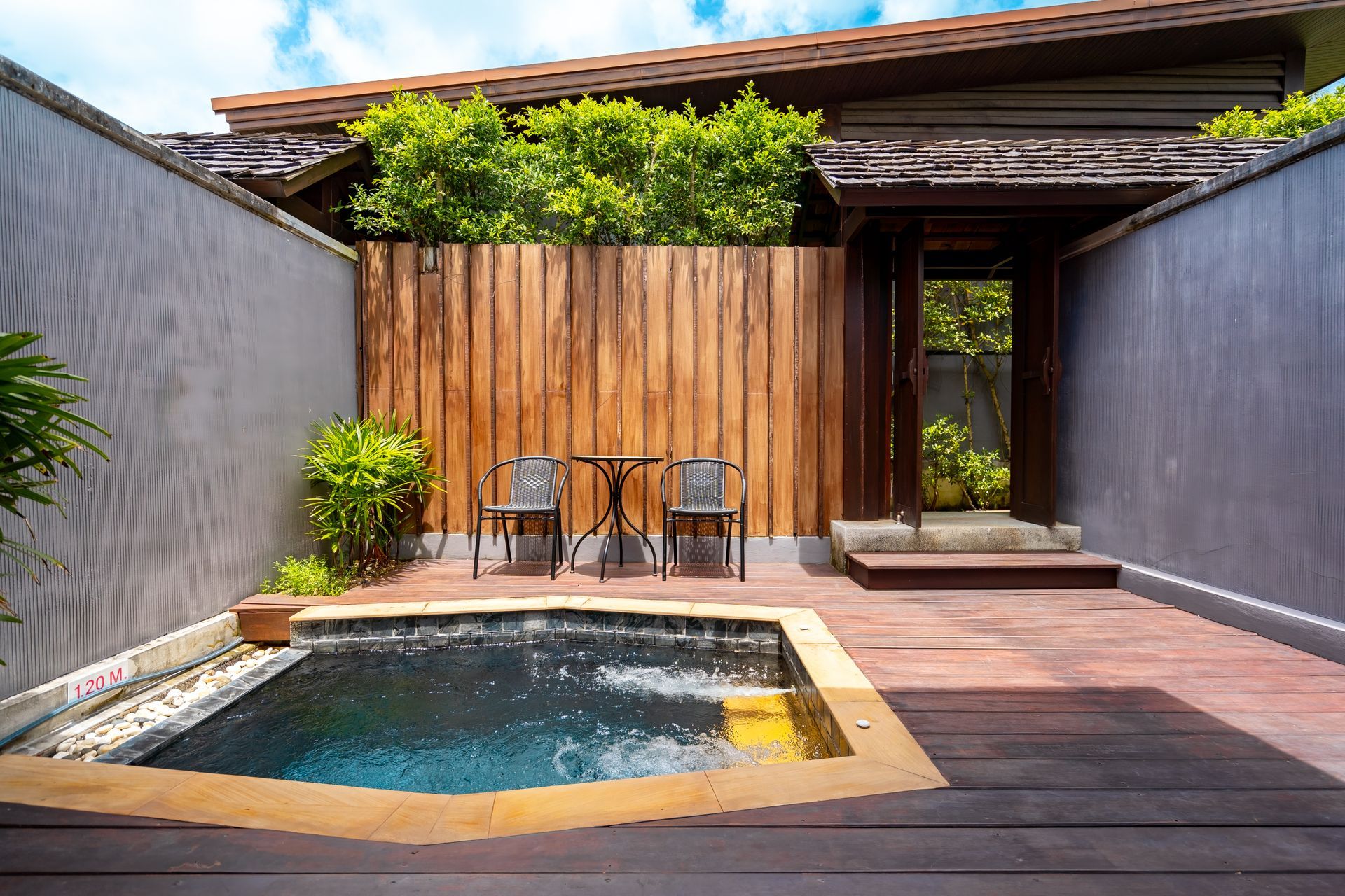 A small swimming pool is surrounded by chairs and a wooden fence.