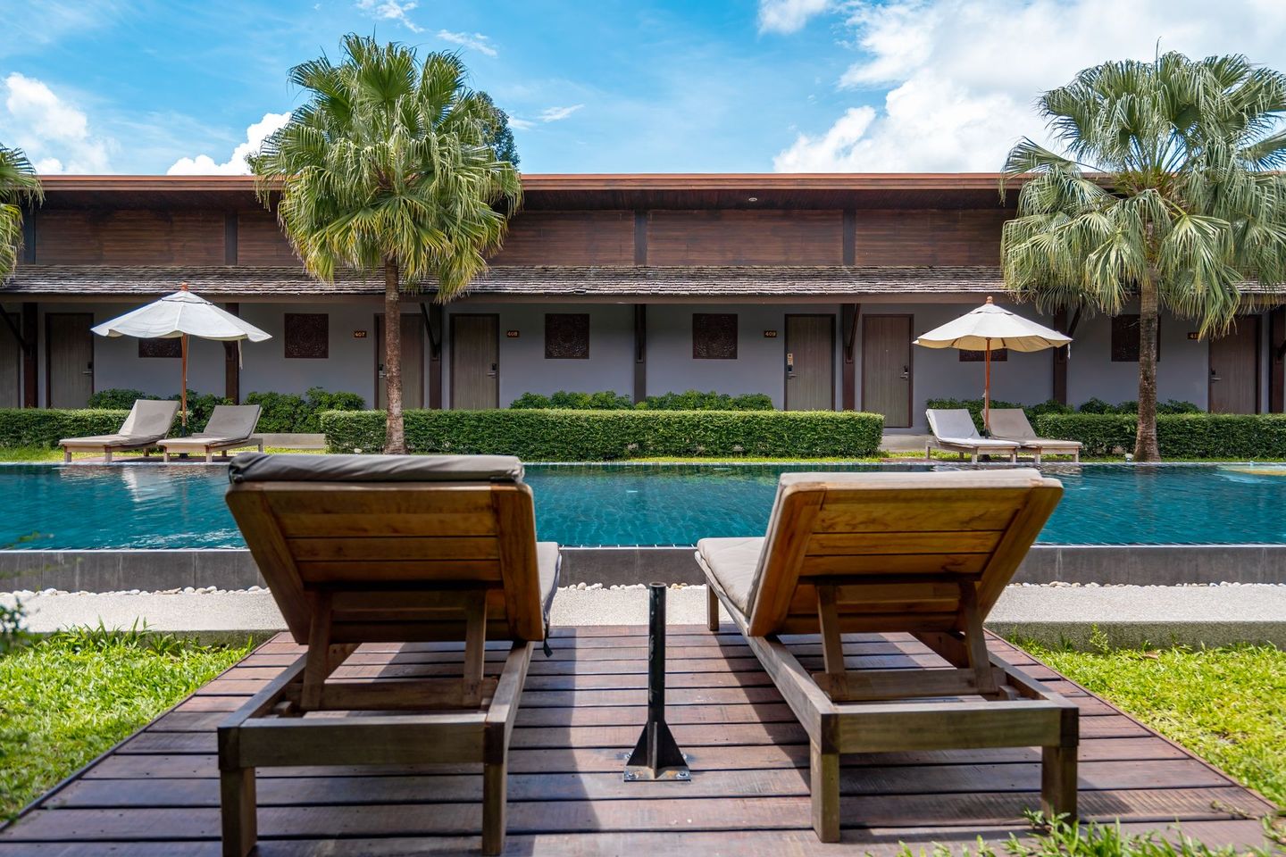 Two wooden lounge chairs are sitting on a wooden deck next to a swimming pool.