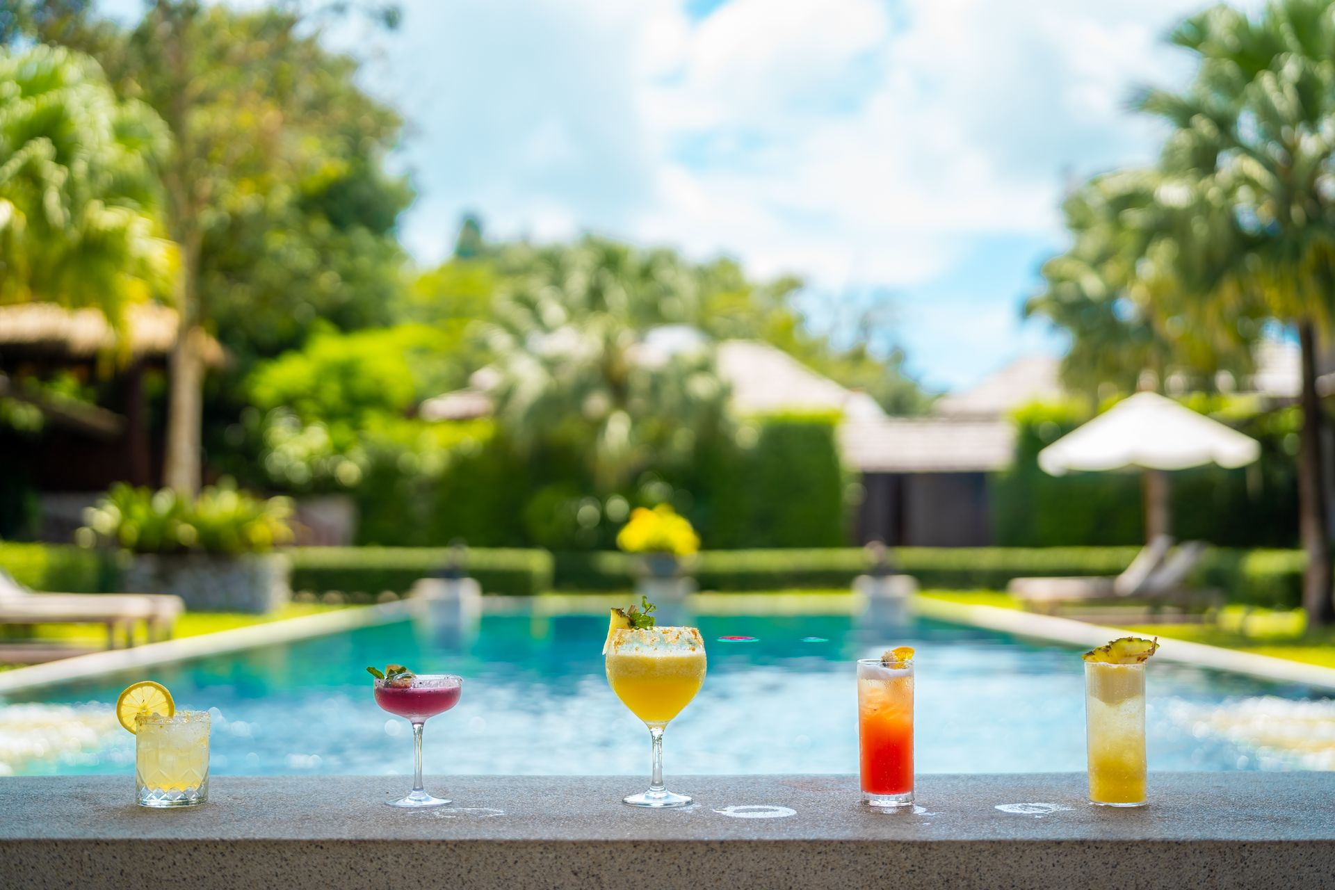 A row of drinks sitting on a bar next to a swimming pool.