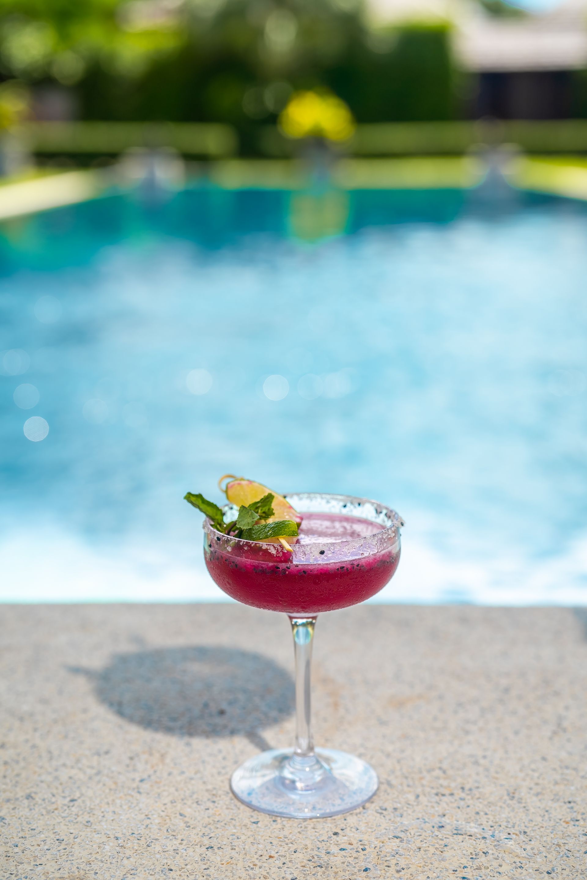 A red cocktail is sitting on the edge of a swimming pool.