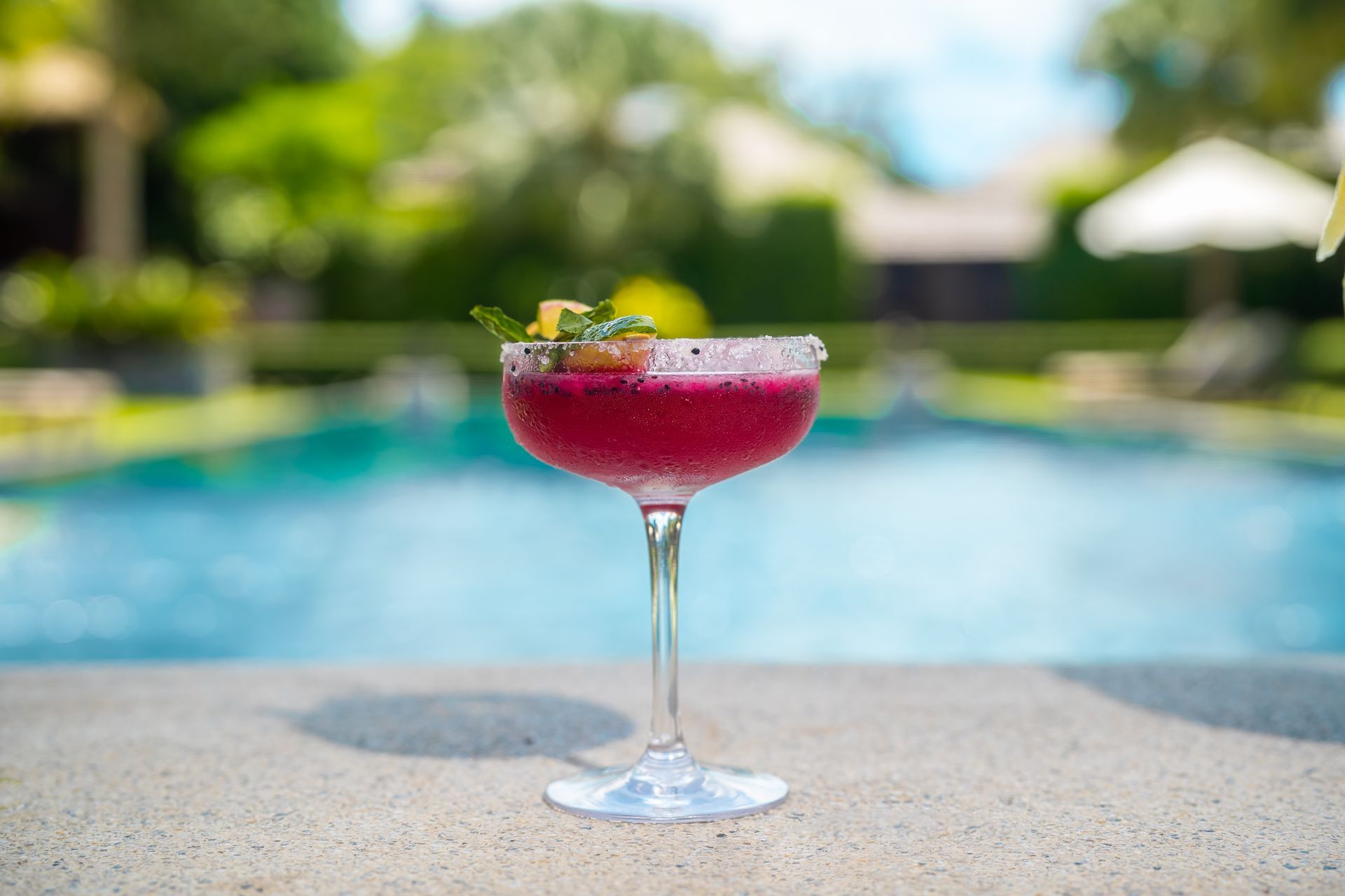 A red cocktail is sitting on the edge of a swimming pool.