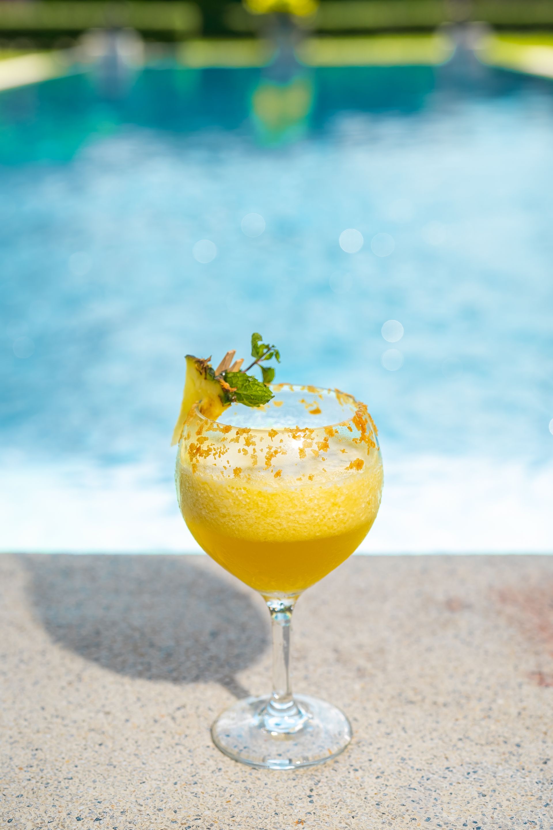 A close up of a cocktail in a wine glass on the edge of a swimming pool.